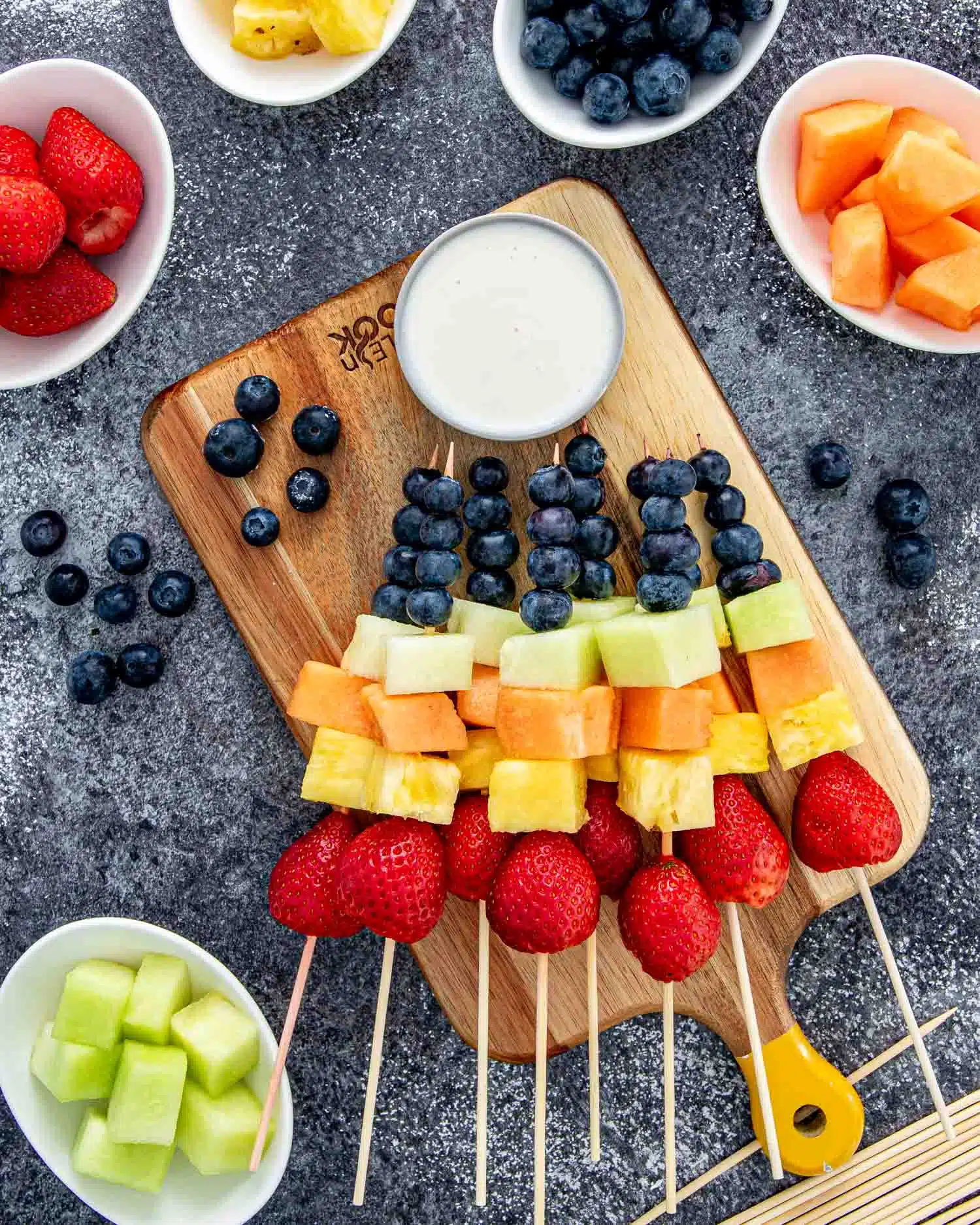 a few rainbow fruit skewers on a cutting board.