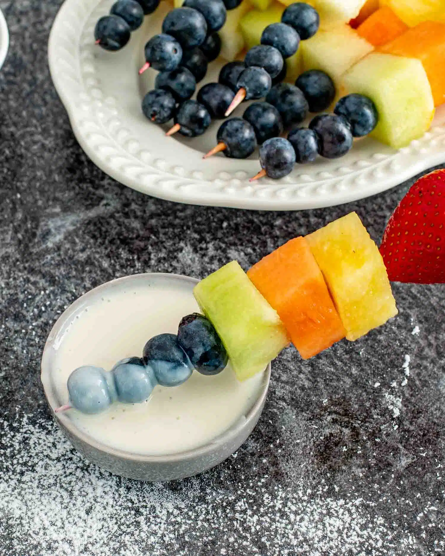 dipping a rainbow fruit skewer in a little dipping bowl with yogurt dip.