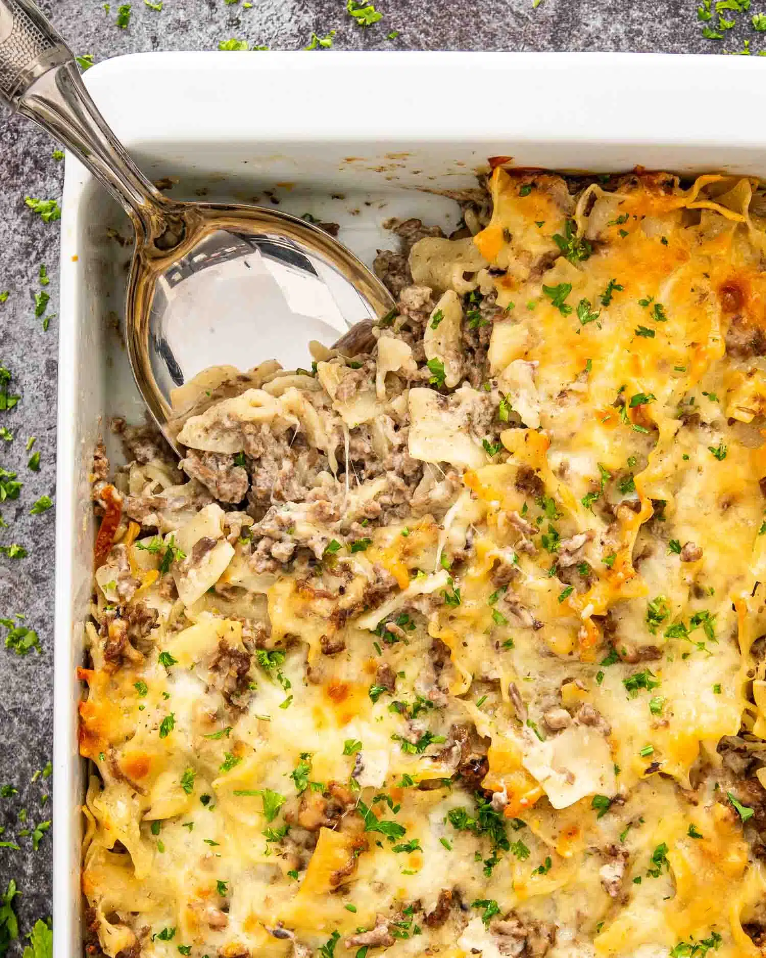 freshly baked beef stroganoff casserole in a white casserole dish garnished with parsley.