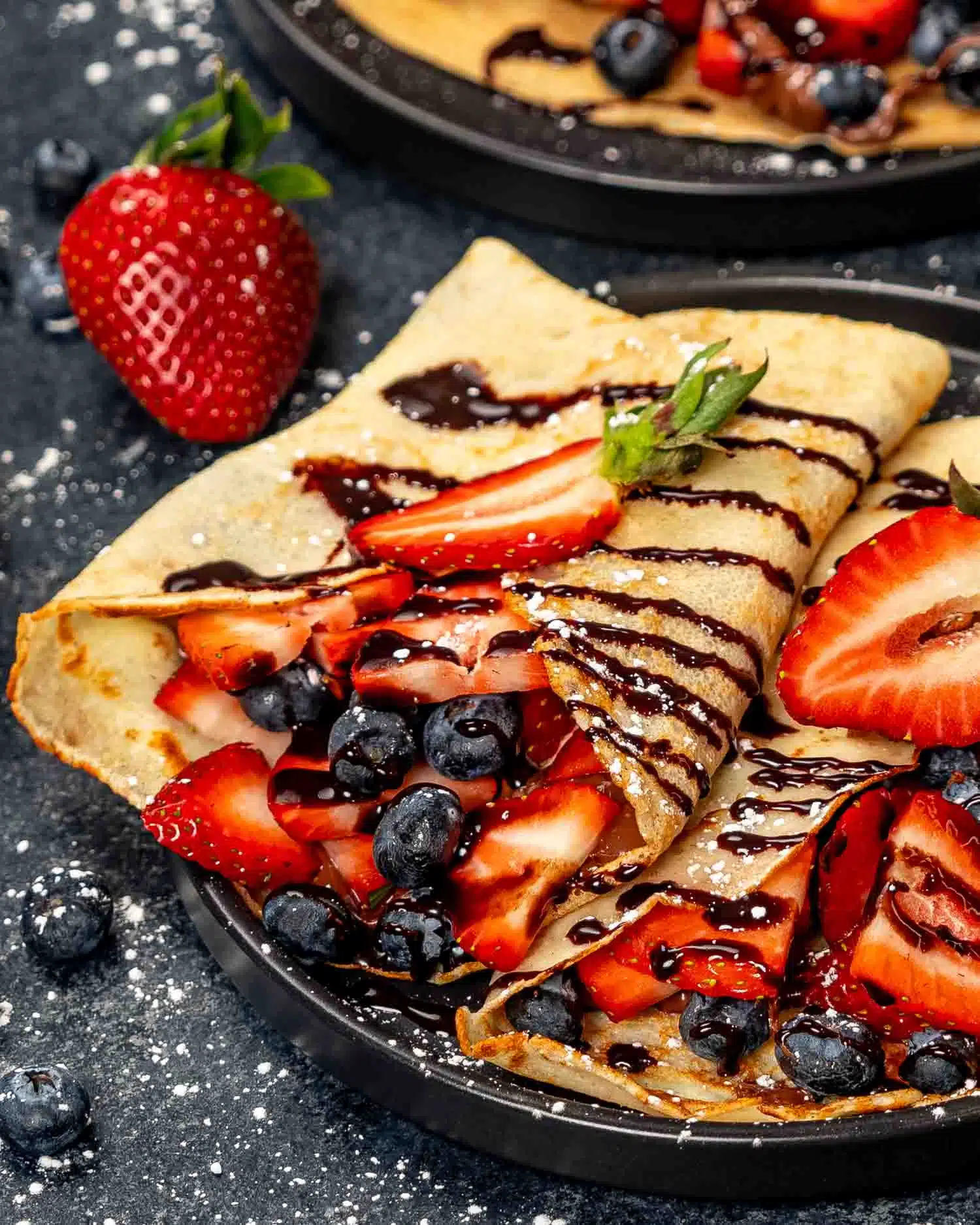 two crepes stuffed with nutella and berries on a black plate.
