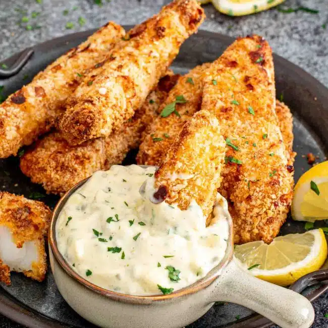 air fried fish sticks on a platter with a bowl with tartar sauce in it.