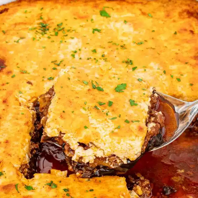 freshly baked moussaka in a white casserole dish garnished with parsley.