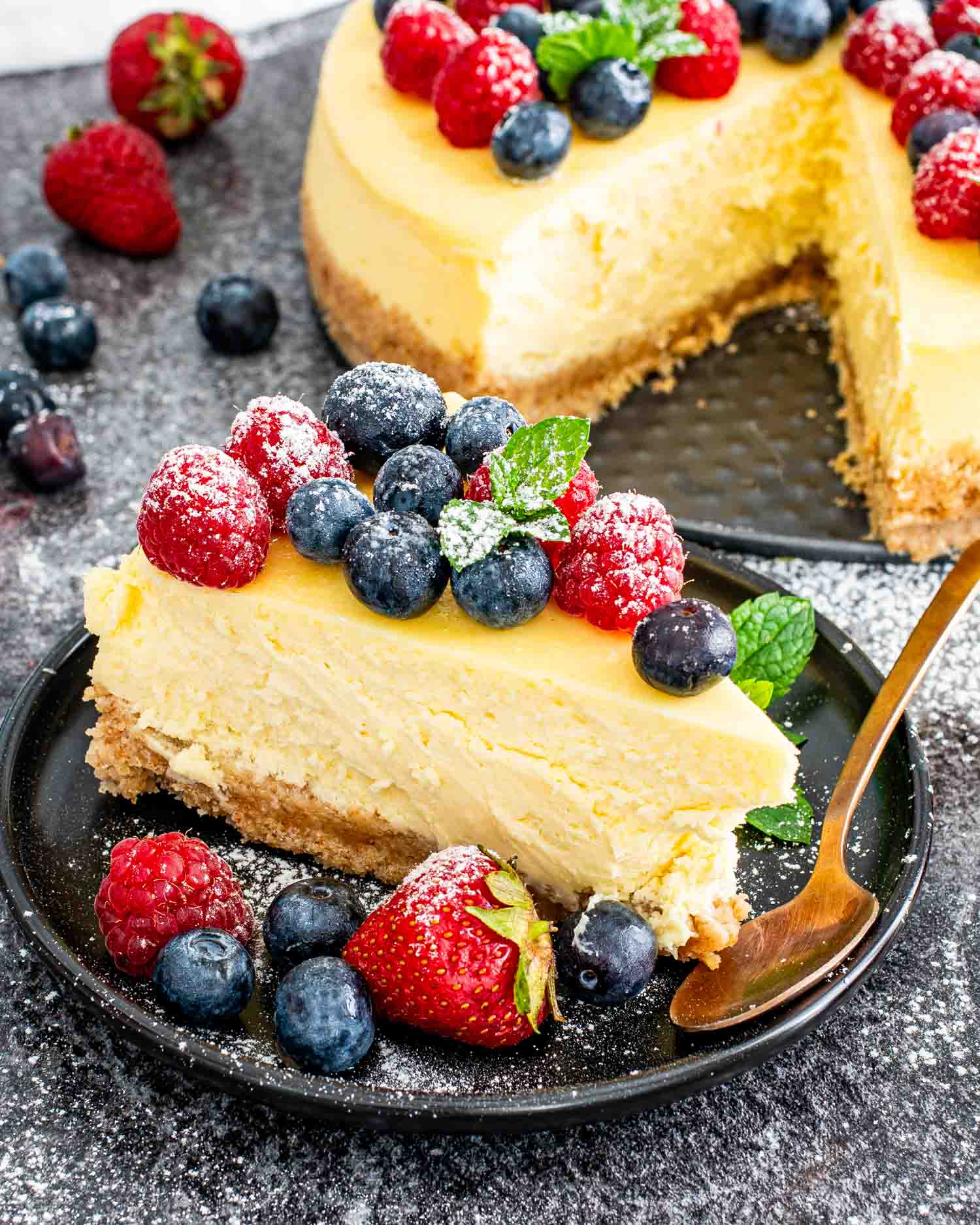 a slice of new york style cheesecake topped with berries on a black plate.