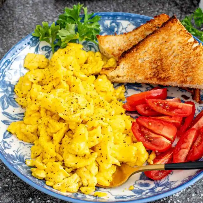 scrambled eggs with tomatoes and toast on a blue plate.