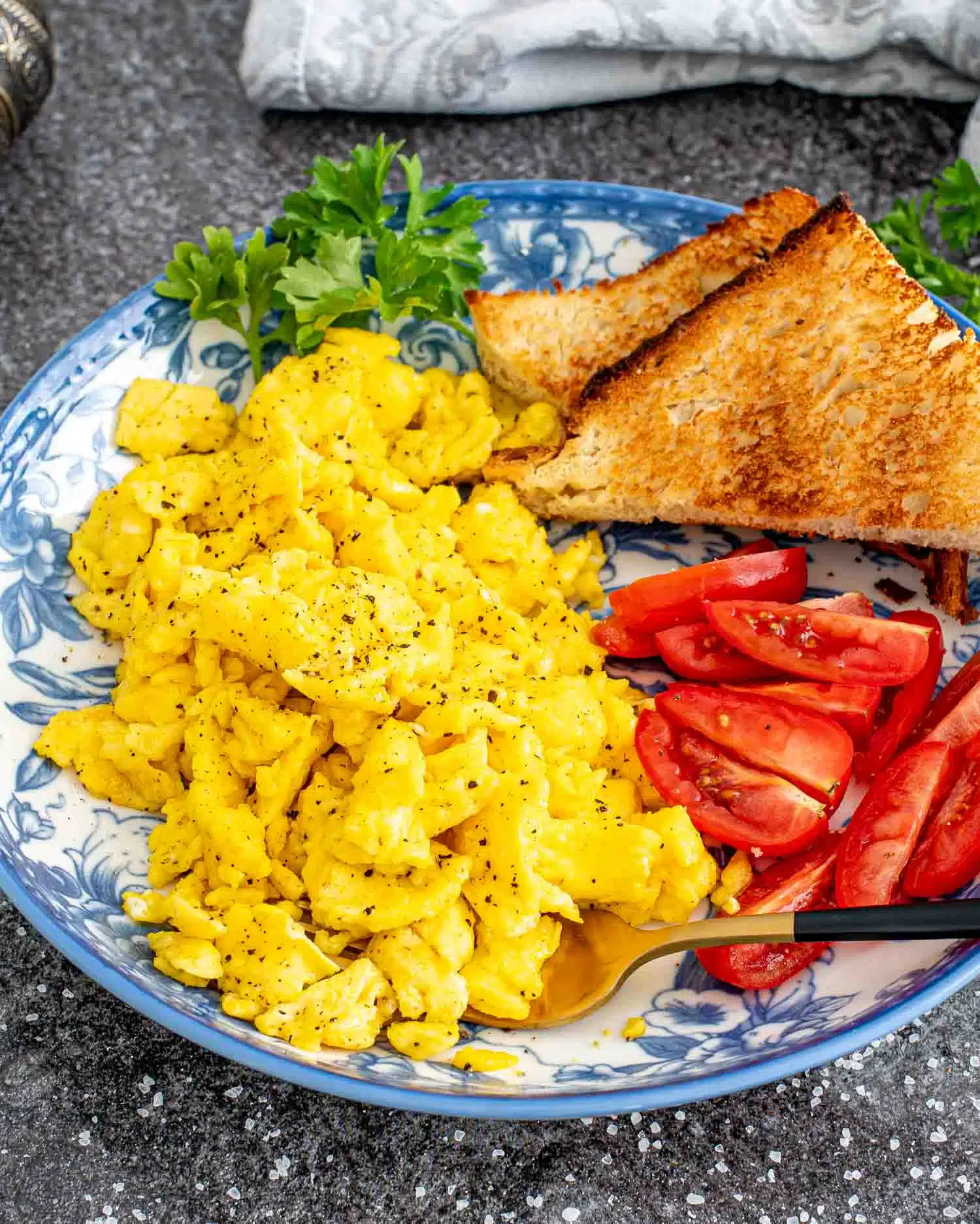 scrambled eggs with tomatoes and toast on a blue plate.