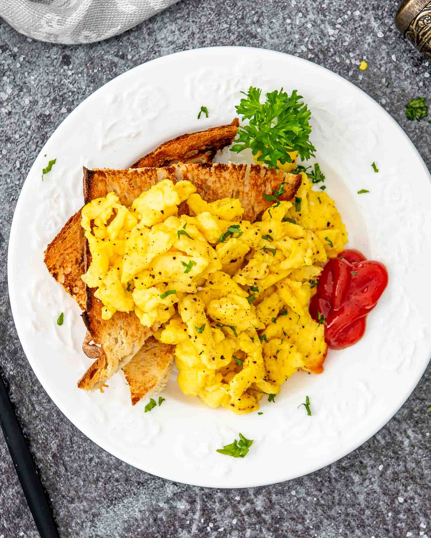 scrambled eggs with ketchup and toast on a white plate.