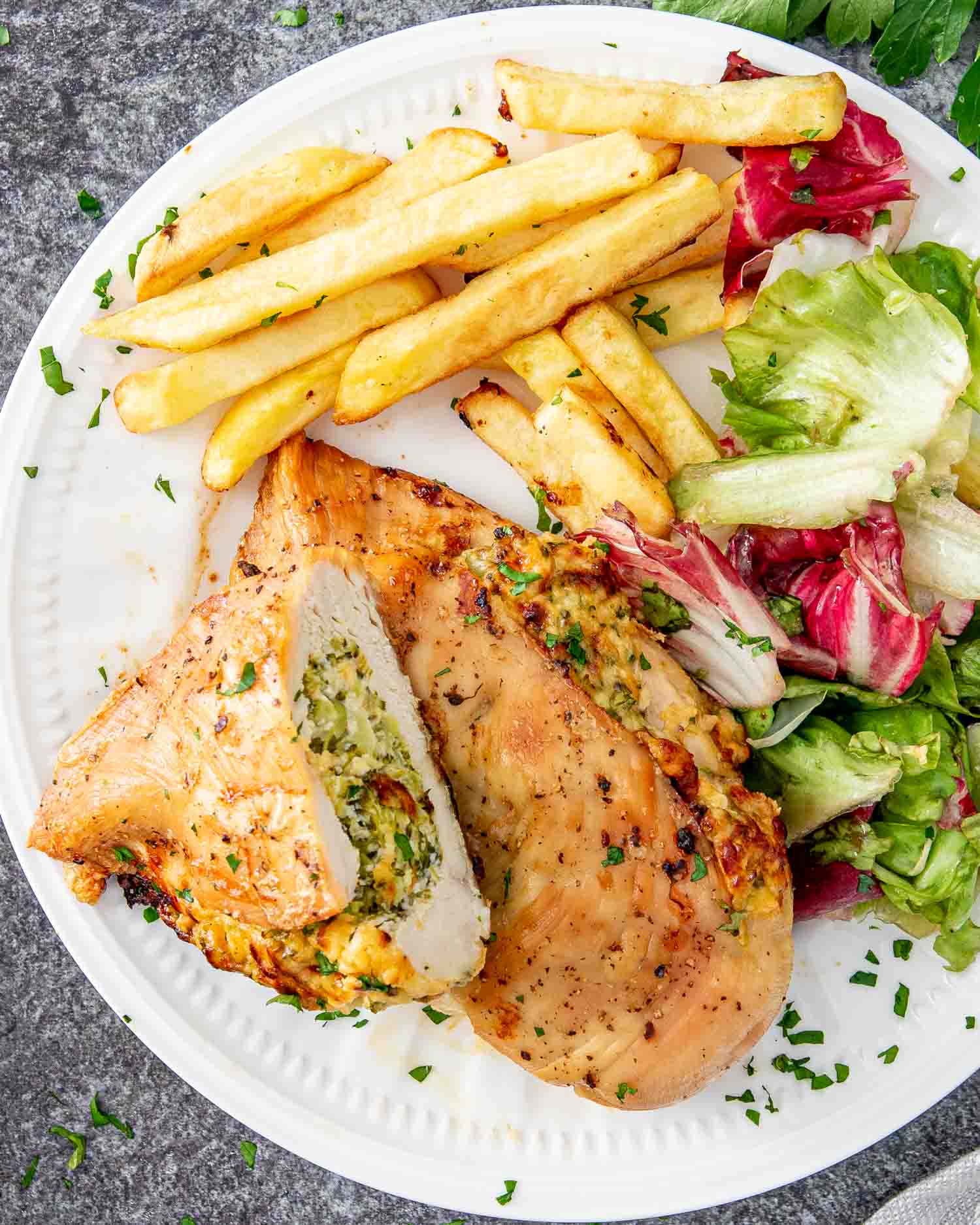 a broccoli cheese stuffed chicken breast on a plate with french fries and a salad.