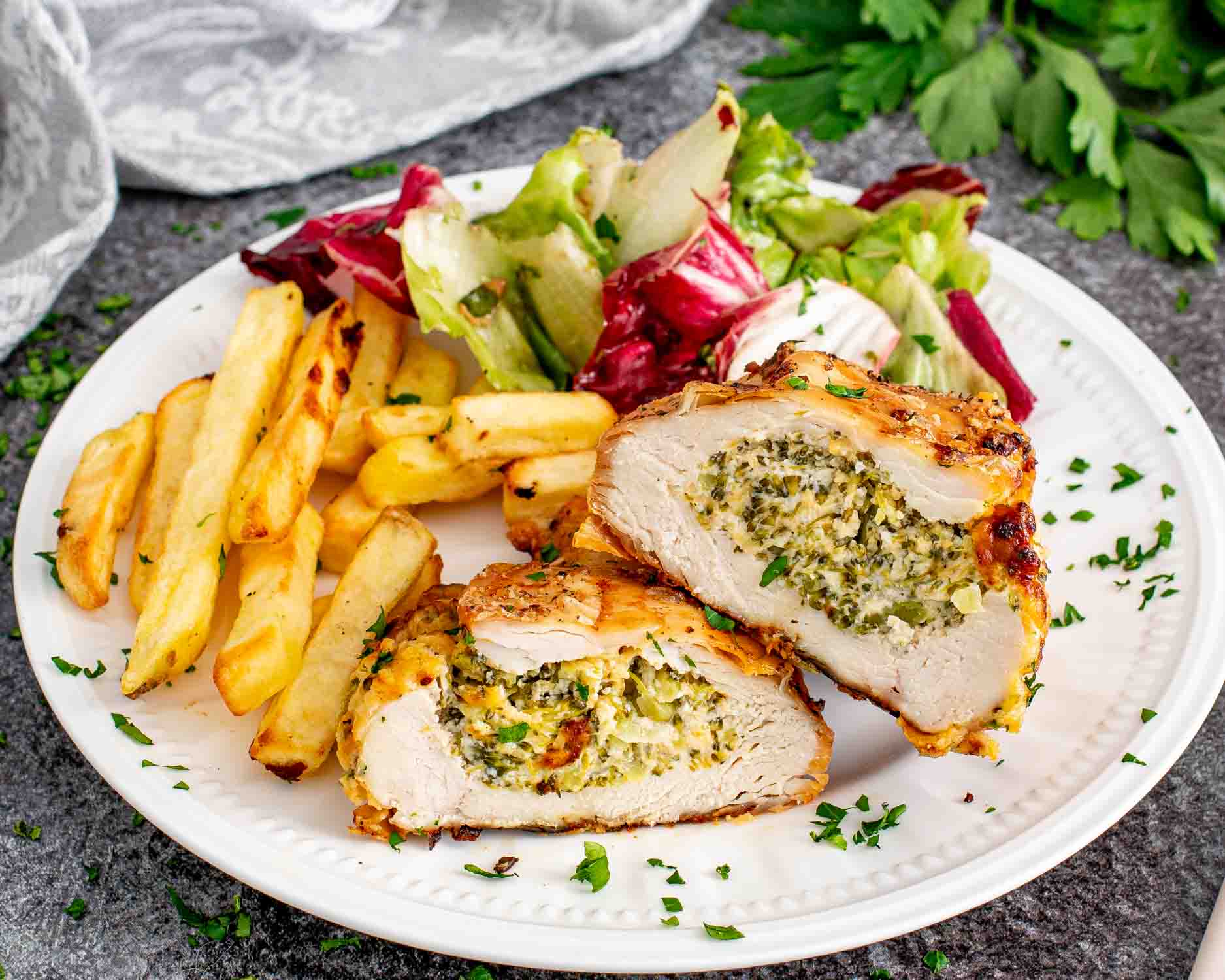 a broccoli cheese stuffed chicken breast cut in half on a plate with french fries and a salad.