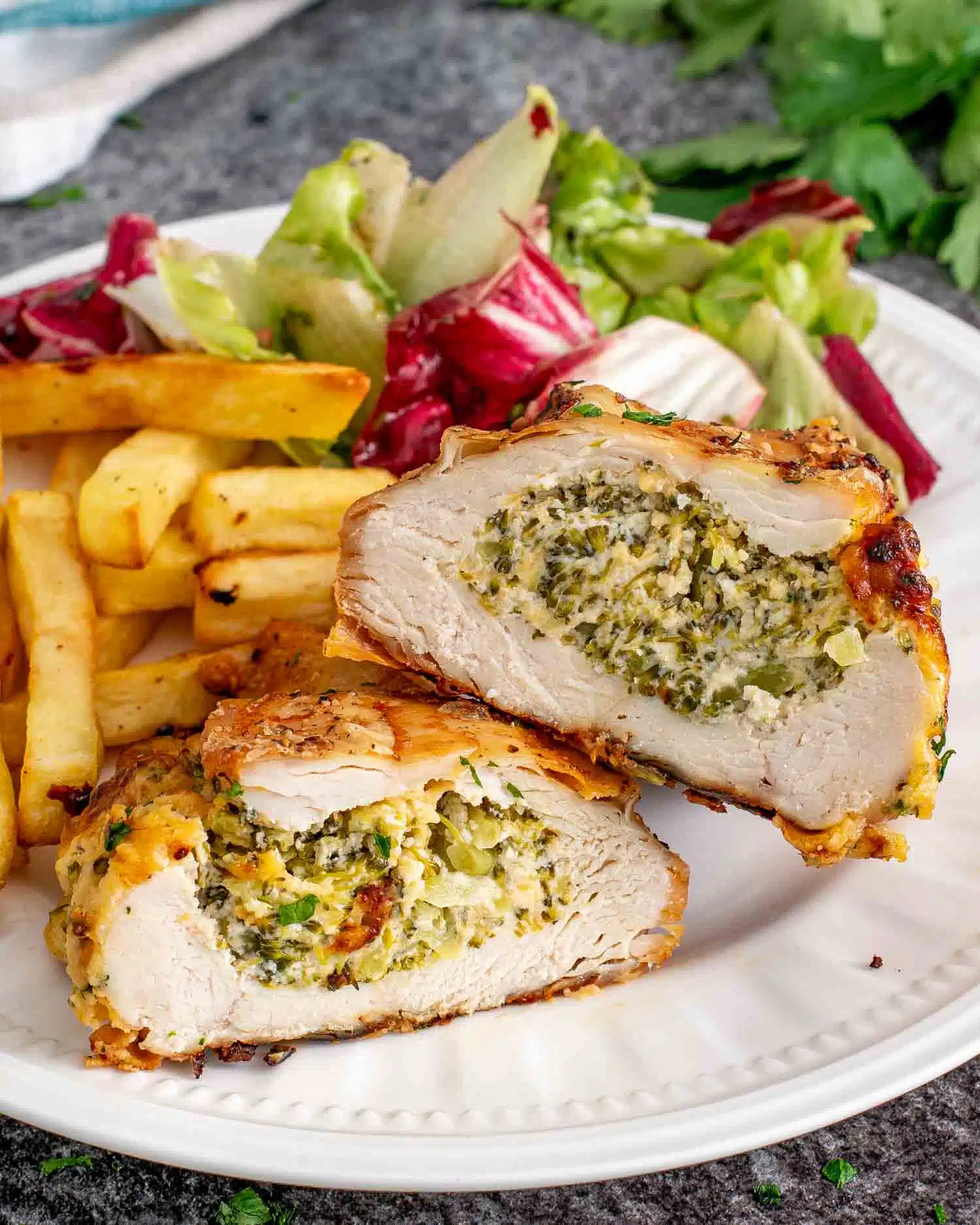 a broccoli cheese stuffed chicken breast cut in half on a plate with french fries and a salad.