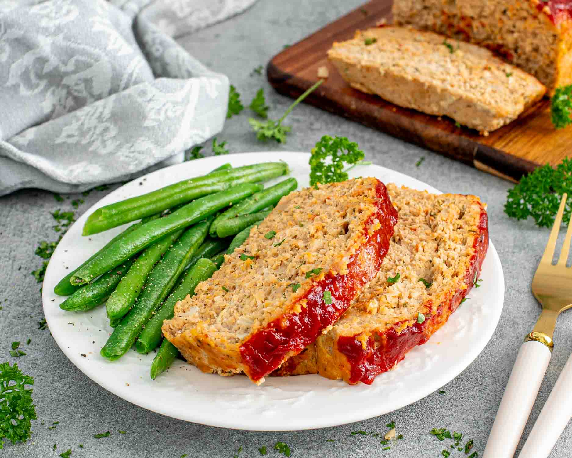 two slices of chicken meatloaf with green beans on a white plate.