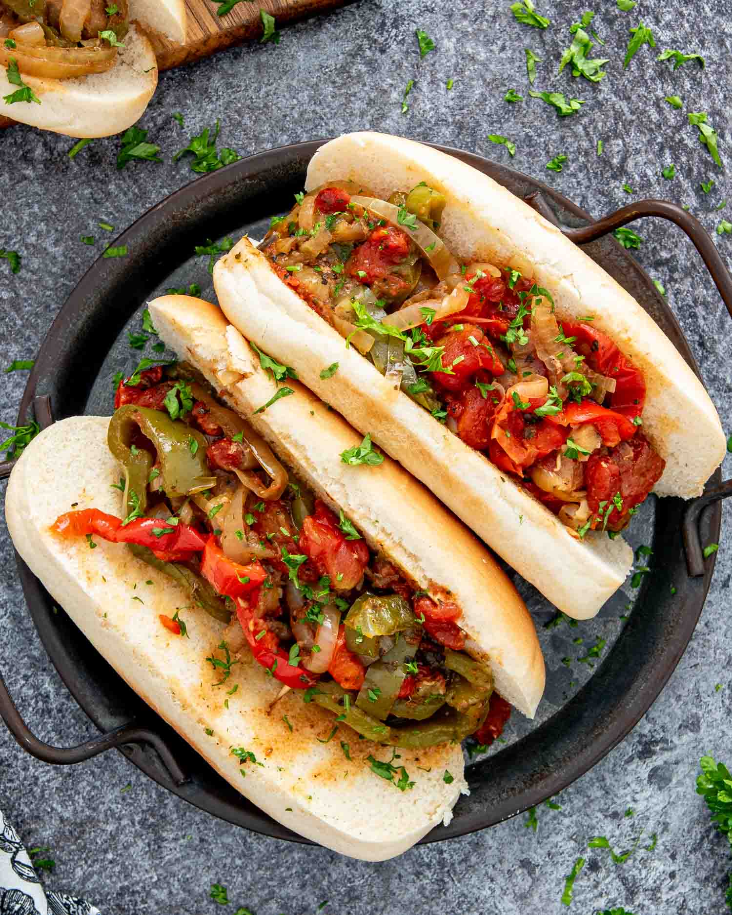 two sausage and peppers hoagie rolls on a plate garnished with some parsley.