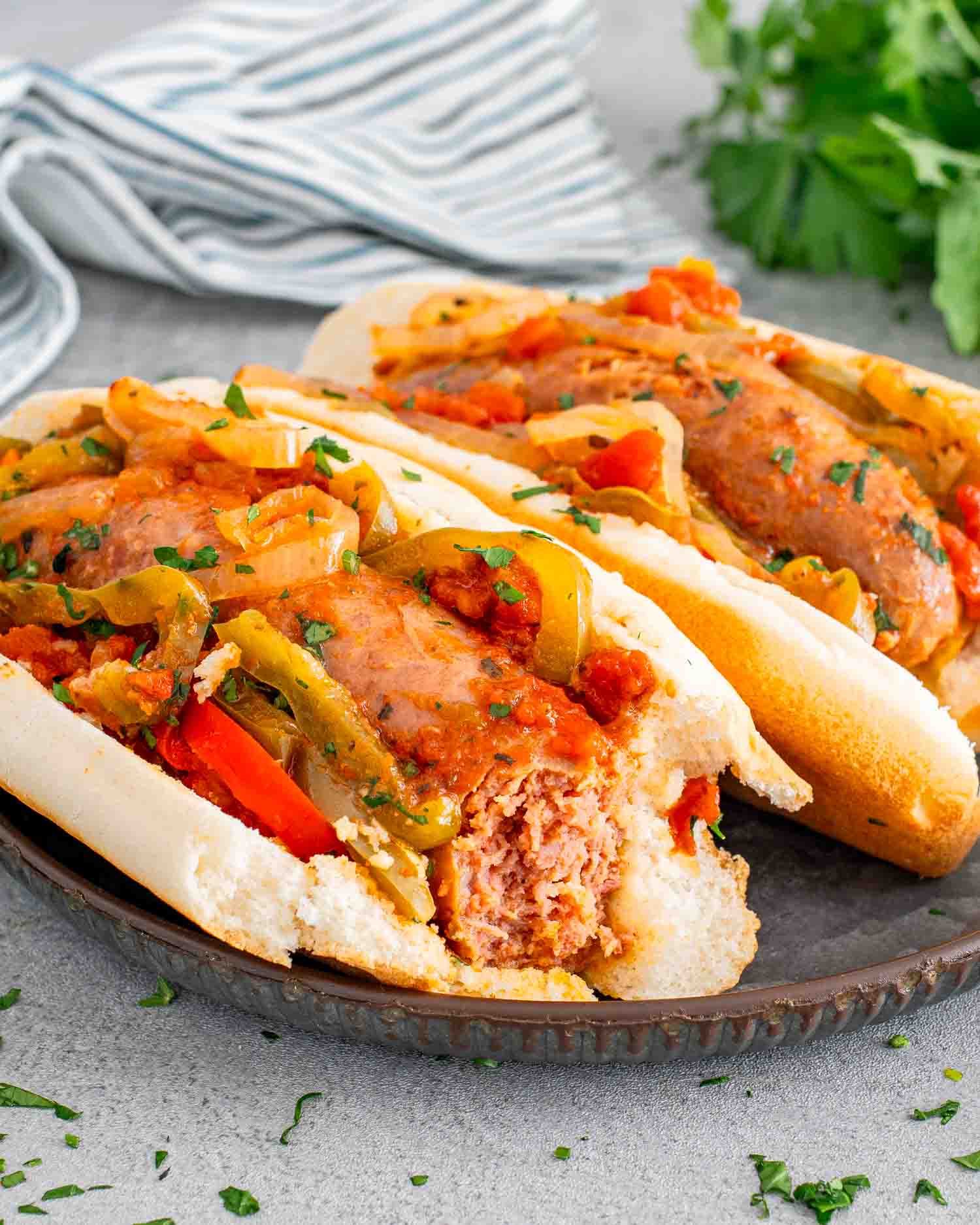 two sausage and peppers hoagie rolls on a plate garnished with some parsley.