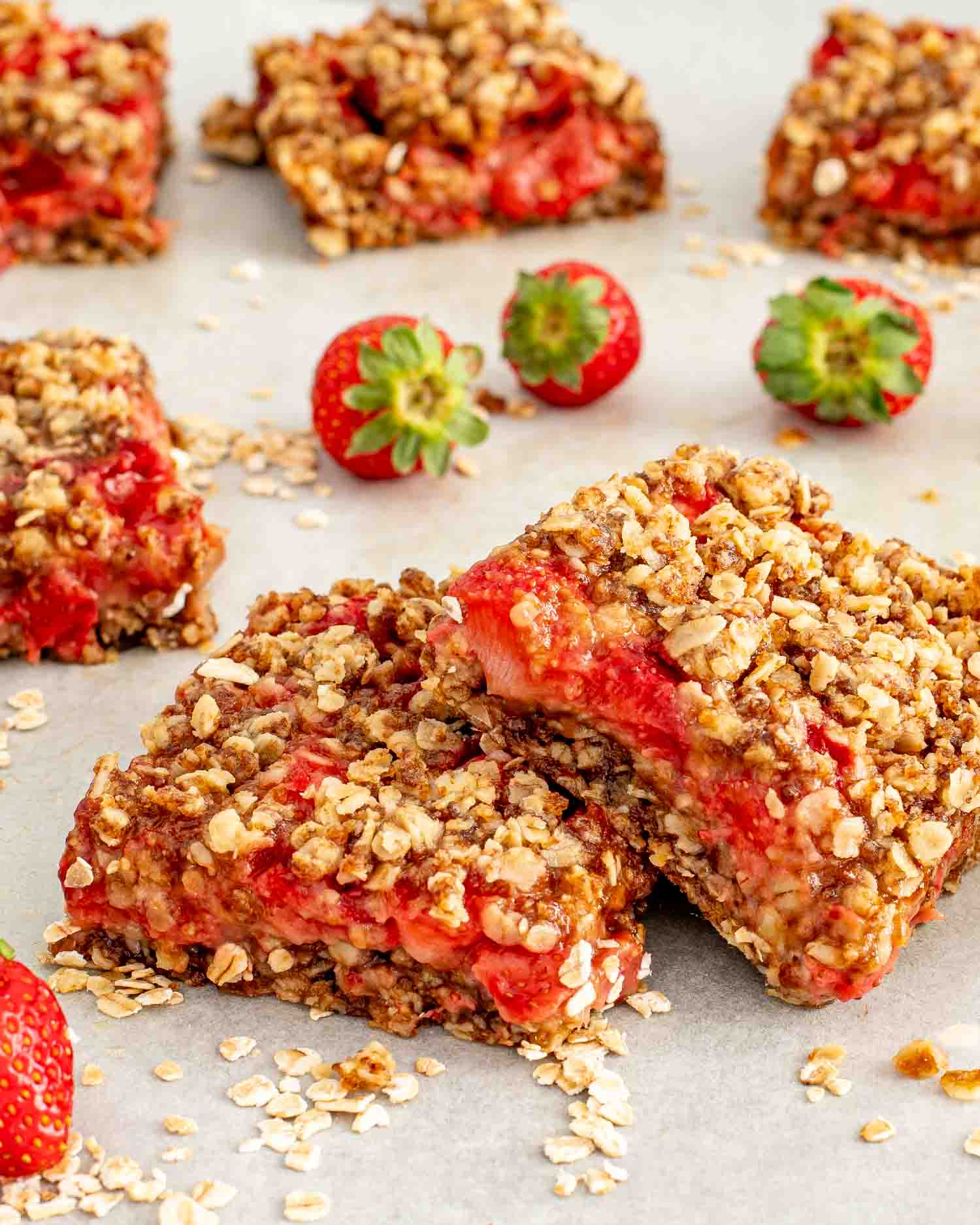 two stacked strawberry oatmeal bars surrounded by fresh strawberries.