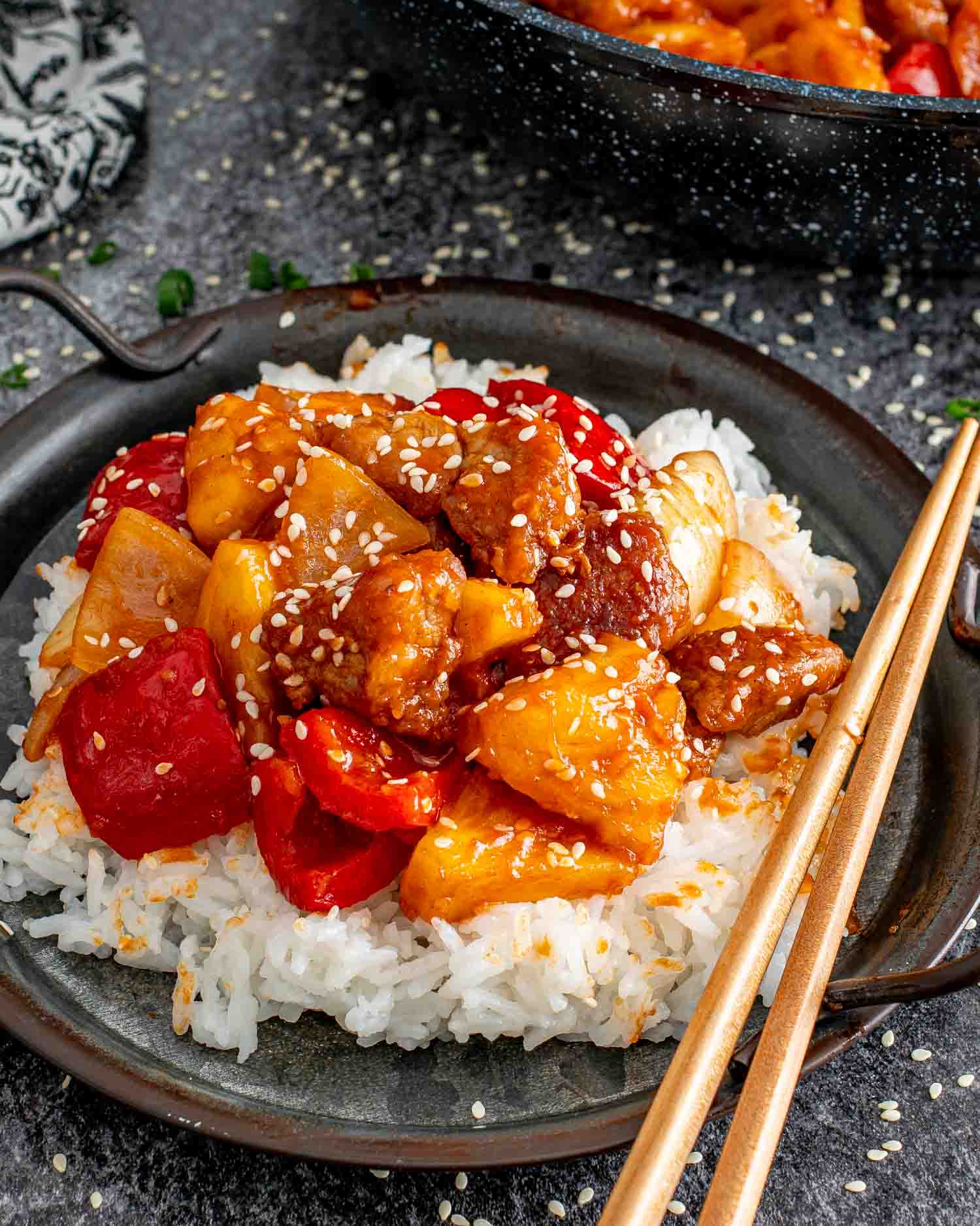 sweet and sour pork in a black plate over a bed of rice.