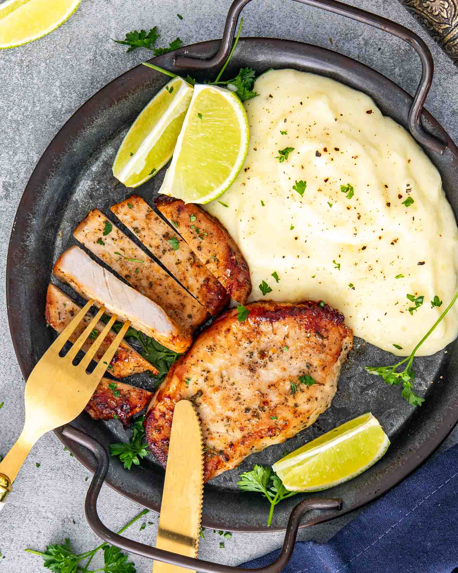 2 ranch pork chops on a plate along some mashed potatoes and garnished with lemon wedges and parsley.