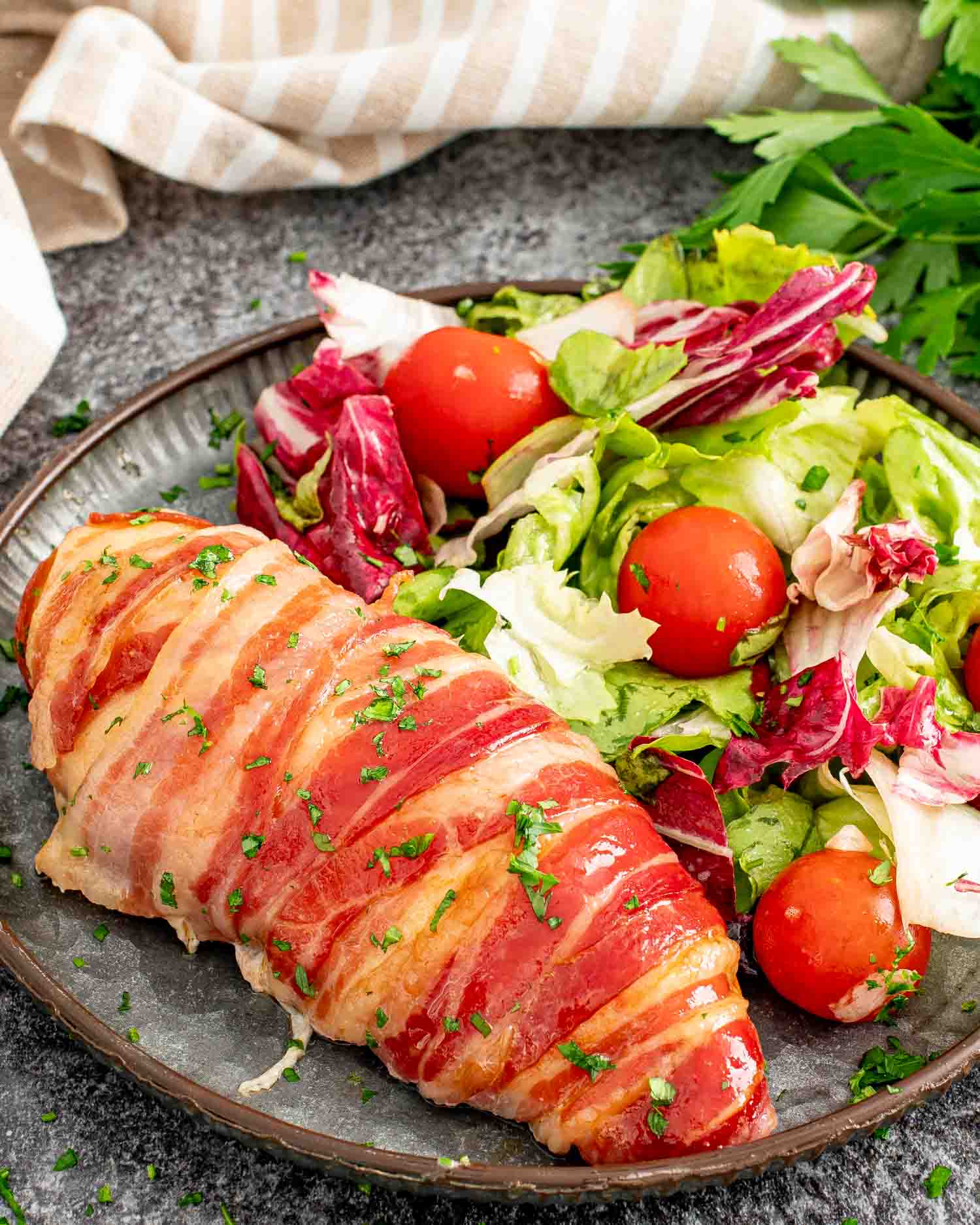 a bacon wrapped chicken breast on a plate along a tossed salad.