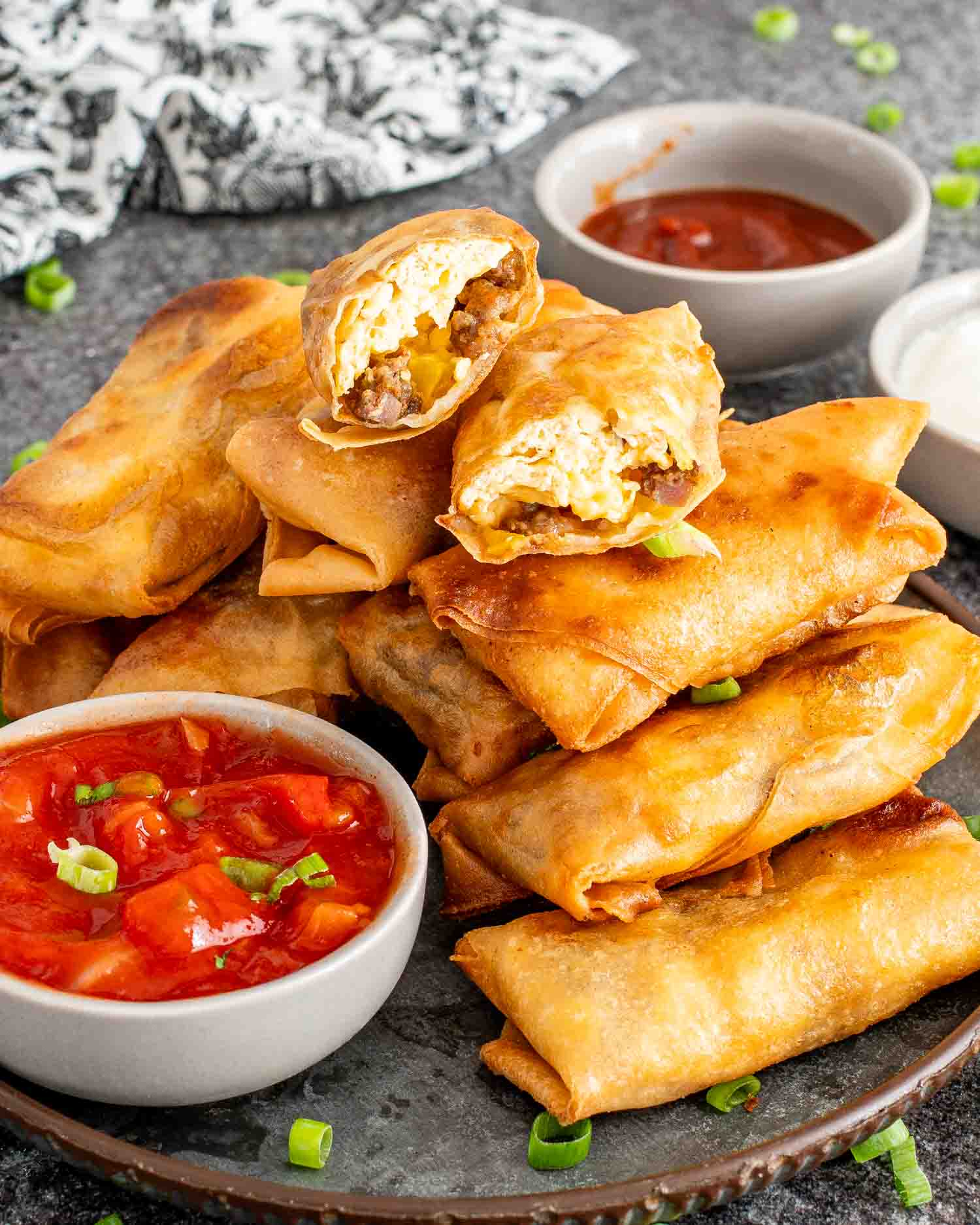 freshly made breakfast egg rolls on a plate along some salsa, ketchup and sour cream.