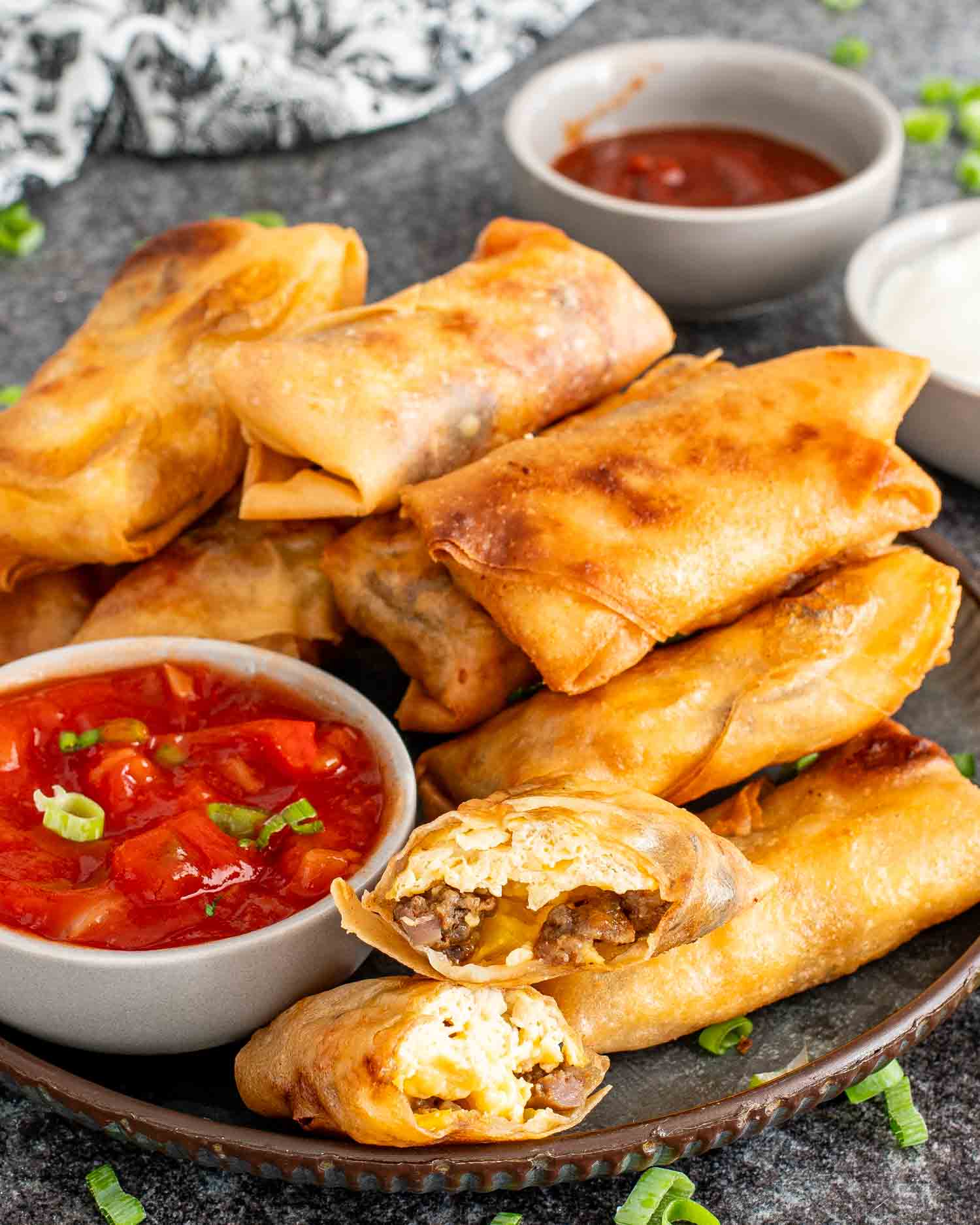 freshly made breakfast egg rolls on a plate along some salsa, ketchup and sour cream.