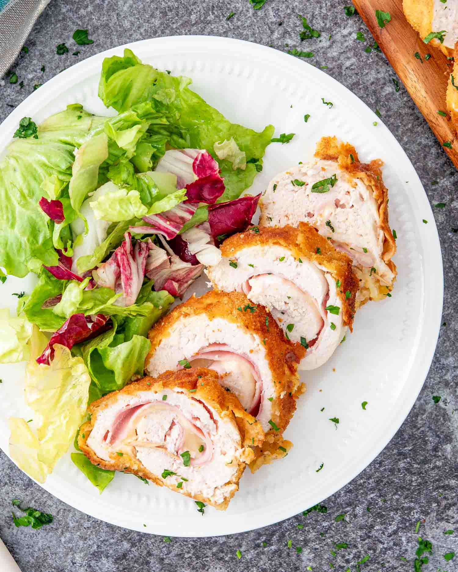 a piece of chicken cordon bleu all sliced up on a plate along a tossed salad.