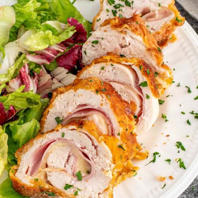 a piece of chicken cordon bleu all sliced up on a plate along a tossed salad.
