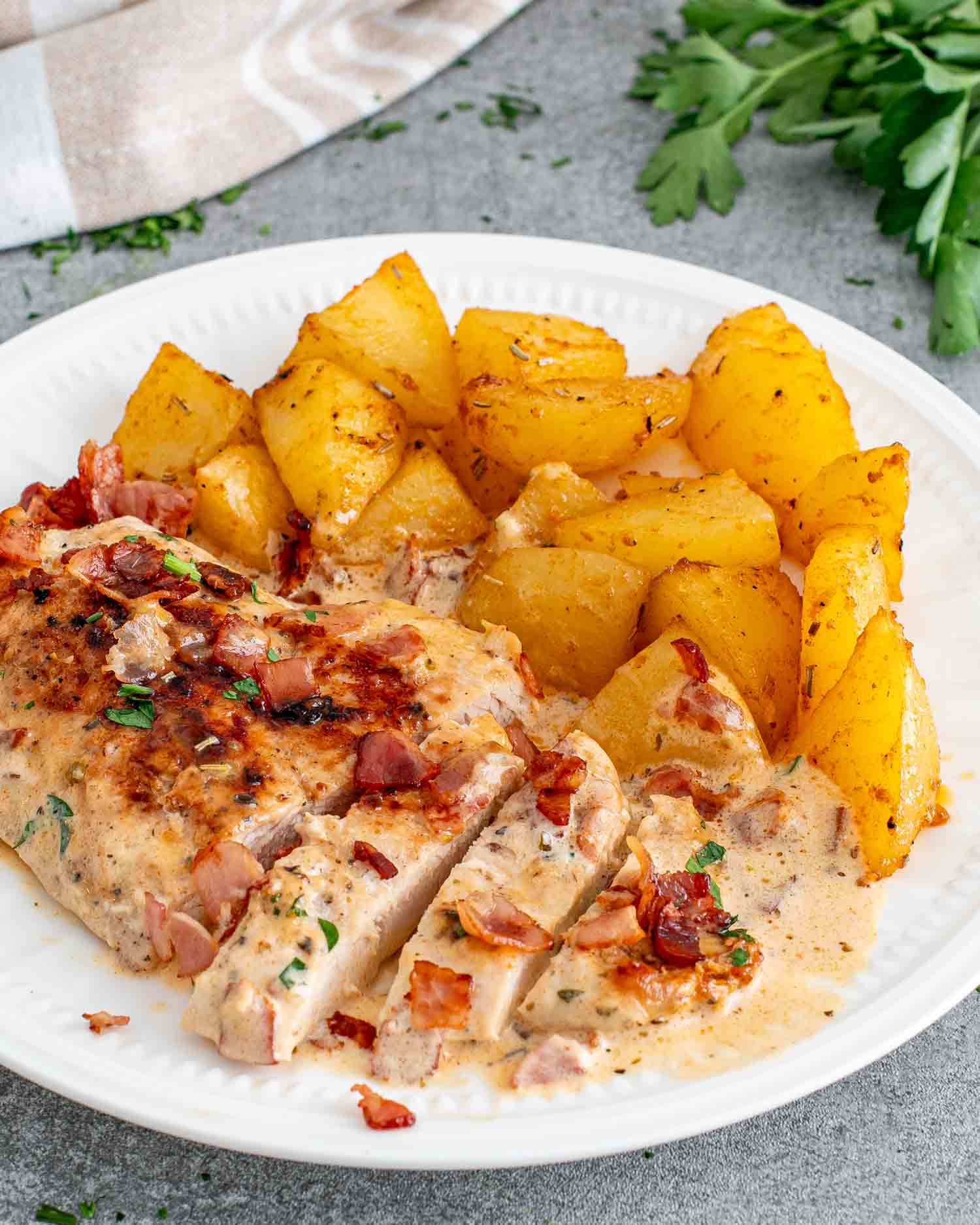 sliced of creamy bacon chicken on a white plate along some roasted potatoes.