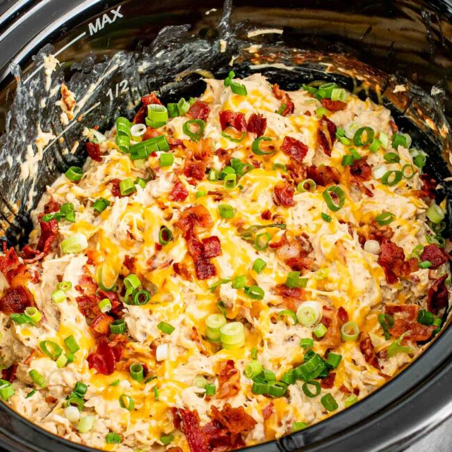 crack chicken in a crockpot, garnished with bacon and green onions.