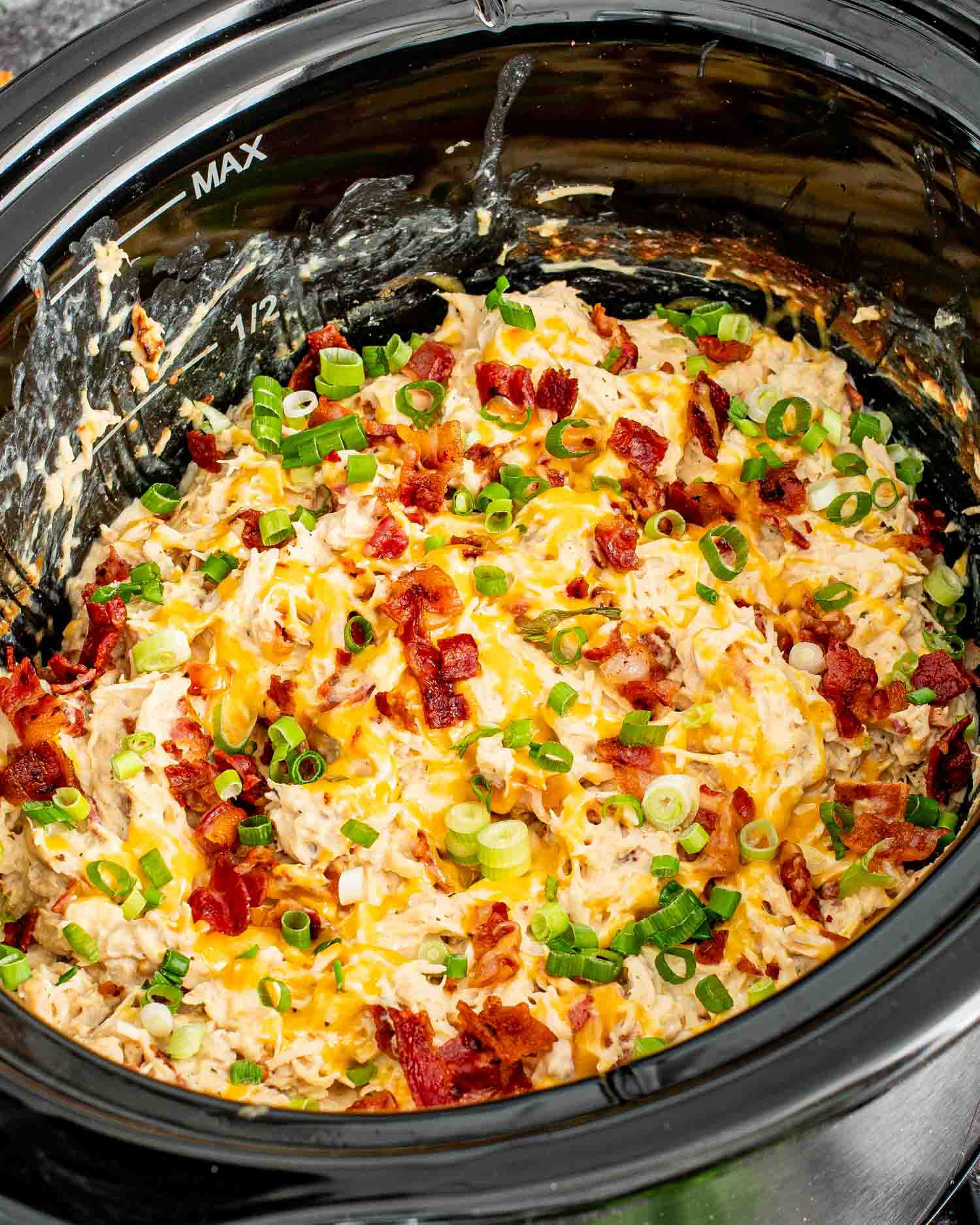 crack chicken in a crockpot, garnished with bacon and green onions.