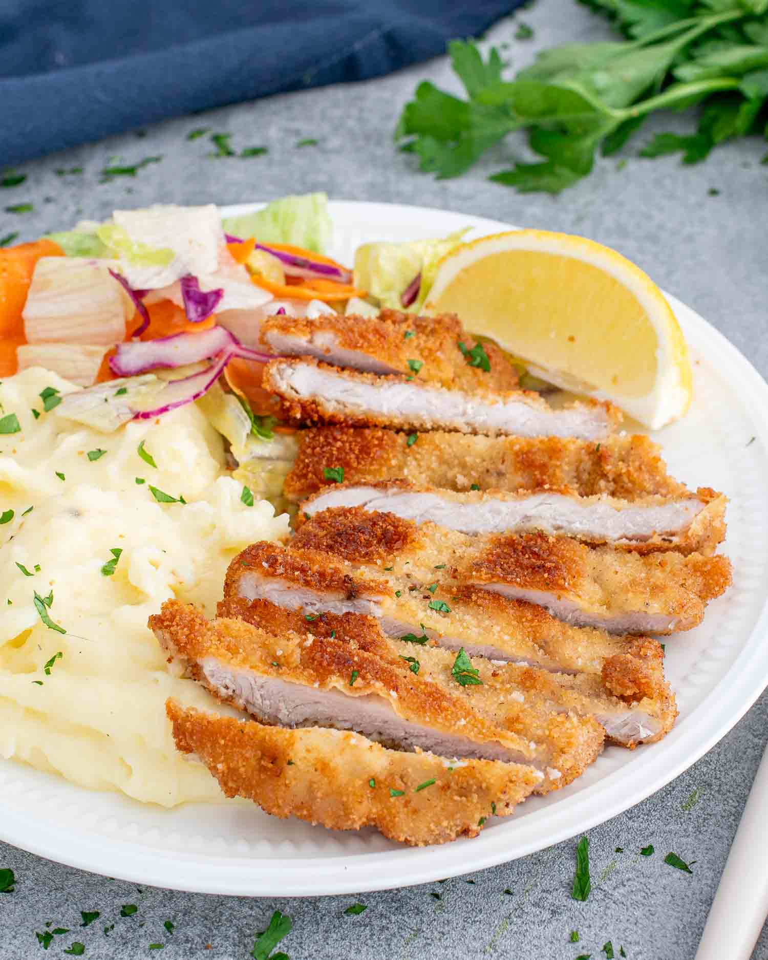 pork schnitzel with mashed potatoes and a tossed salad on a white plate.