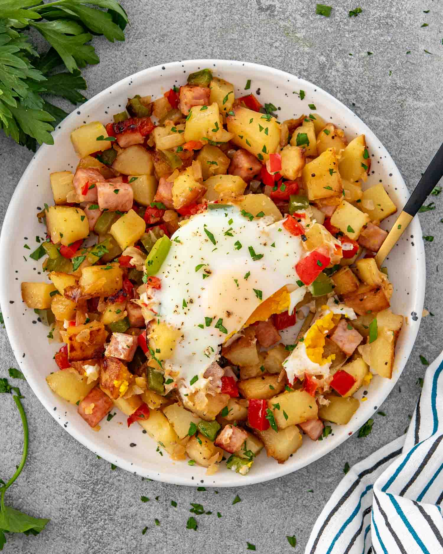 a serving of breakfast hash with an egg on top on a white plate.