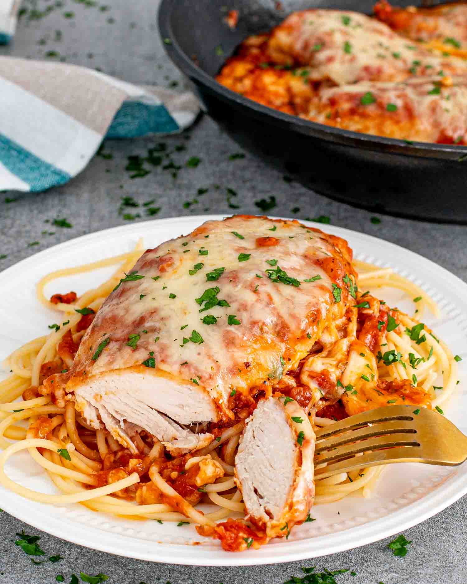 a chicken parmesan breast made in a skillet over a bed of spaghetti garnished with parsley.