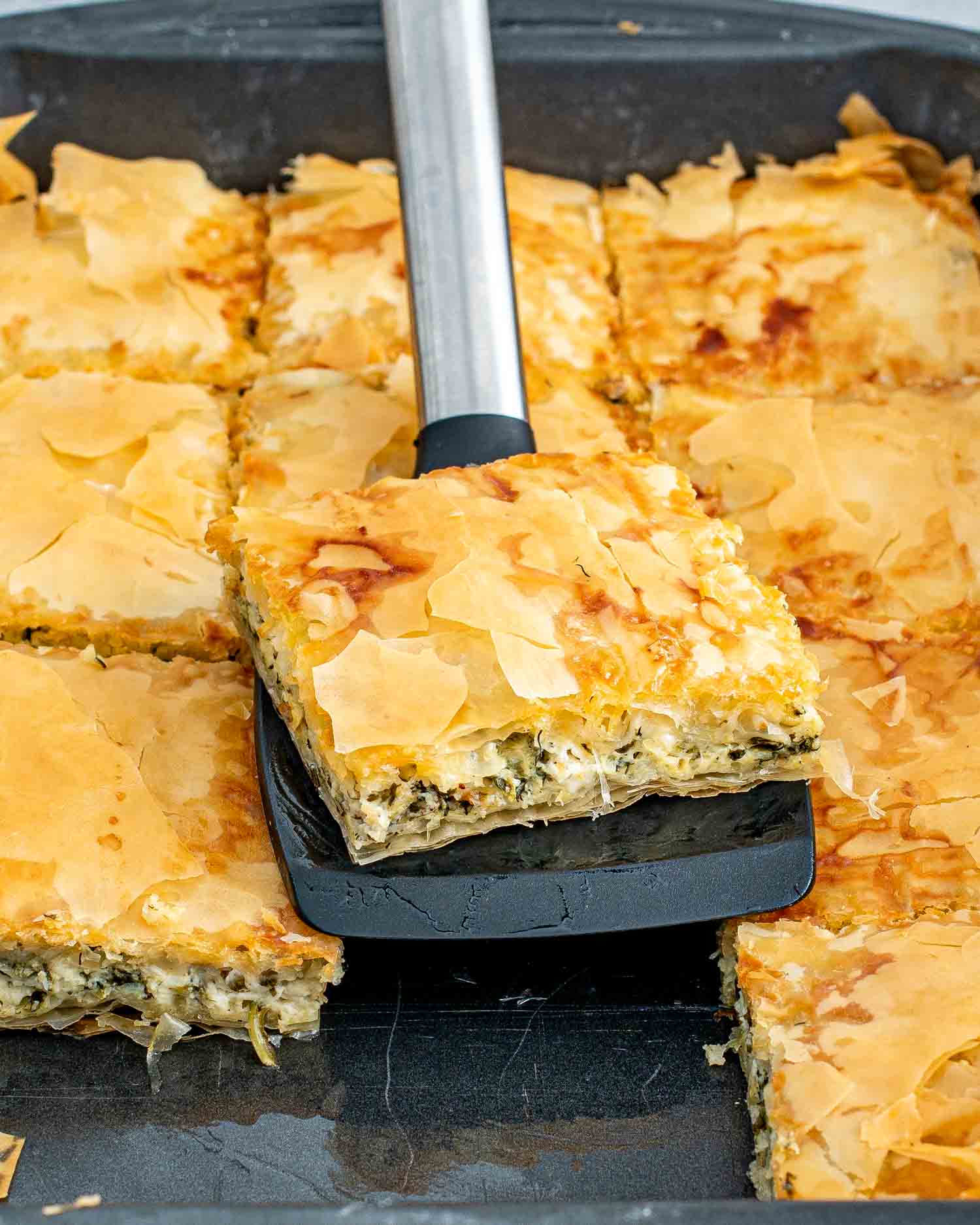 Golden-brown spanakopita with flaky phyllo crust, freshly baked and sliced in a pan.