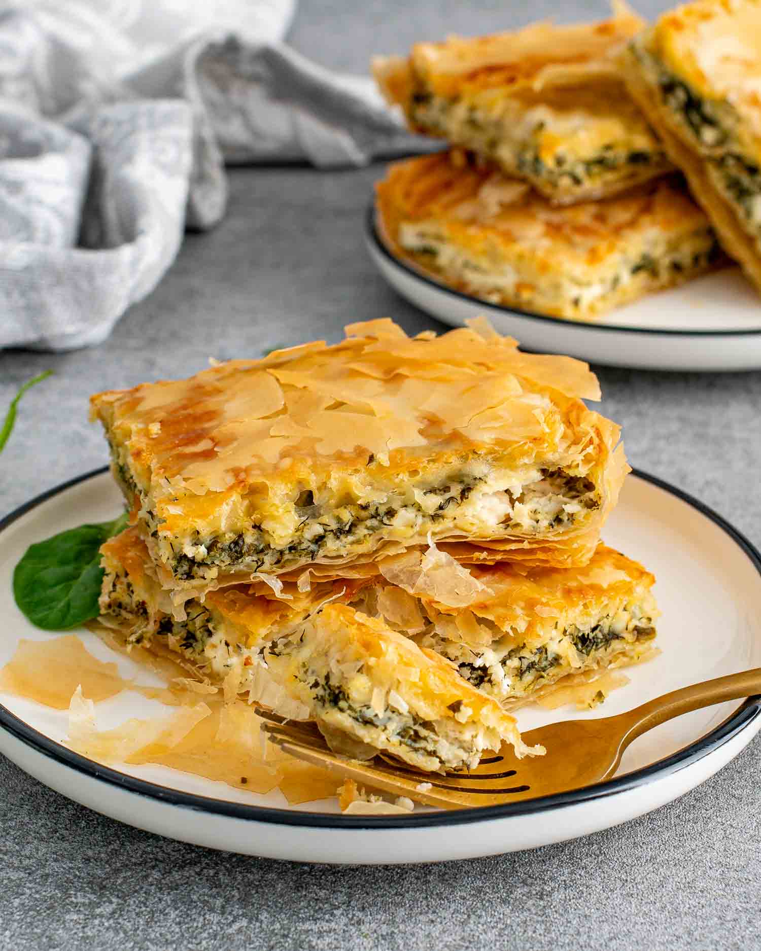 Stacked spanakopita slices on a plate with a fork, ready to eat.
