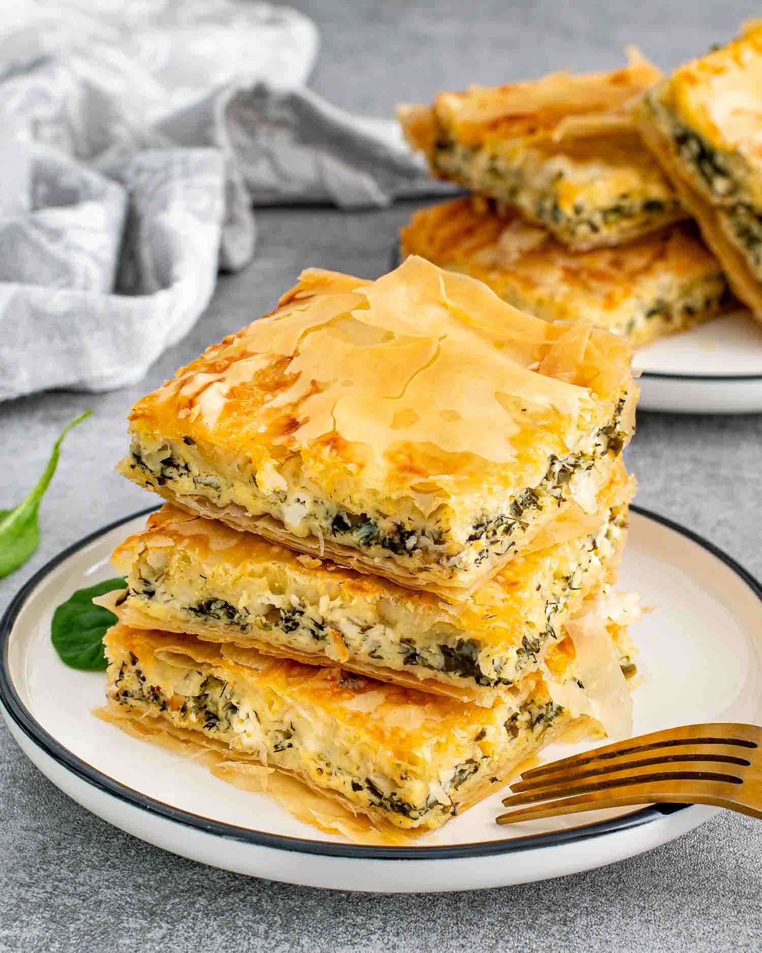 Stacked spanakopita slices on a plate with a fork, ready to eat.