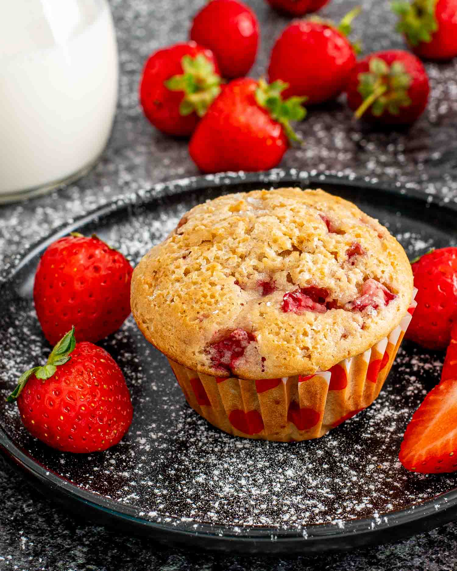 one strawberry muffin on a black plate along side some fresh strawberries.