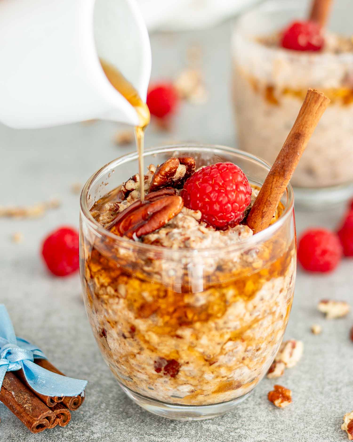 two glasses with maple pecan overnight oats drizzled with maple syrup.