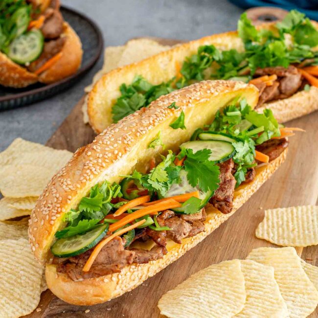 banh mi sandwiches on a cutting board with some chips around it.