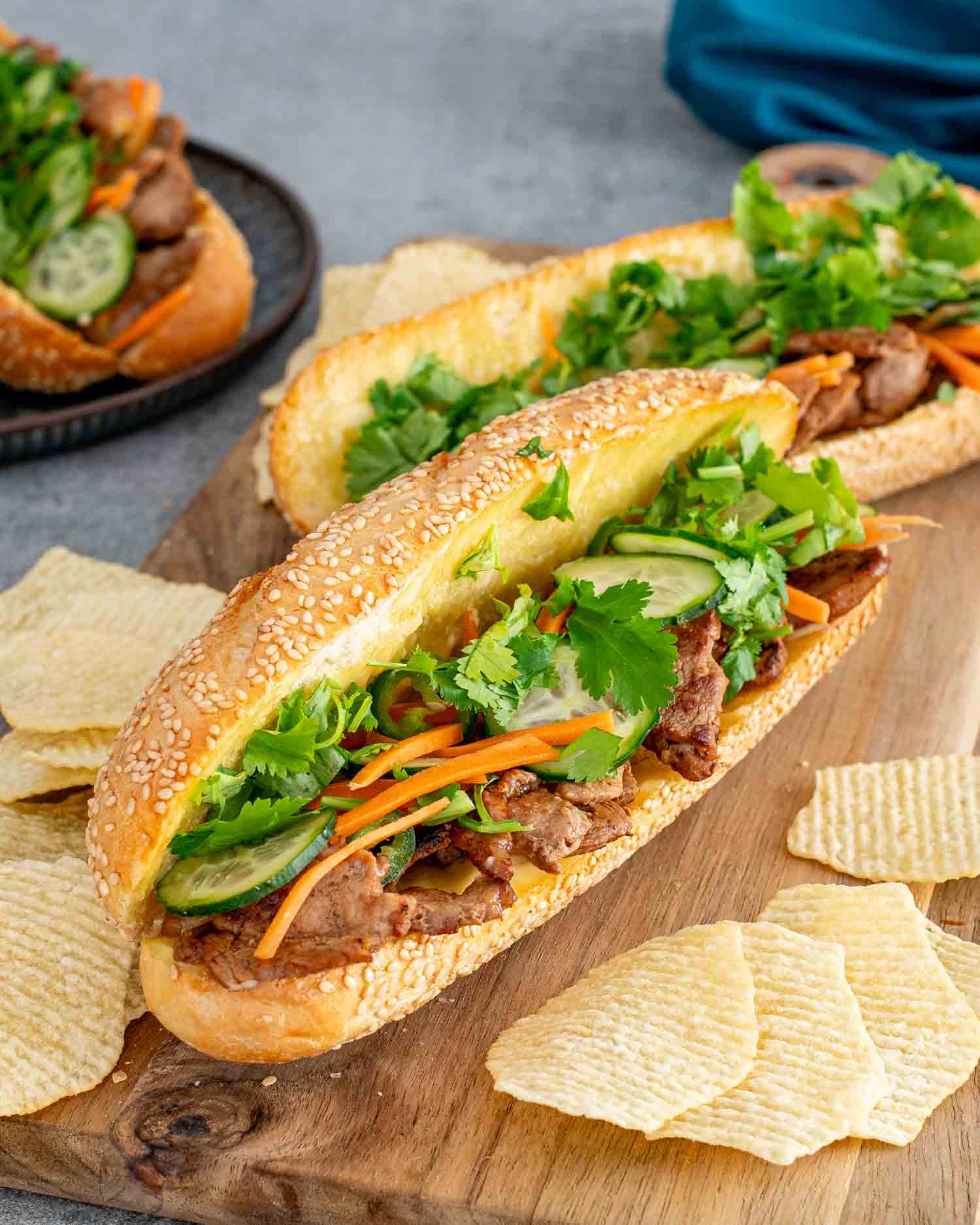banh mi sandwiches on a cutting board with some chips around it.
