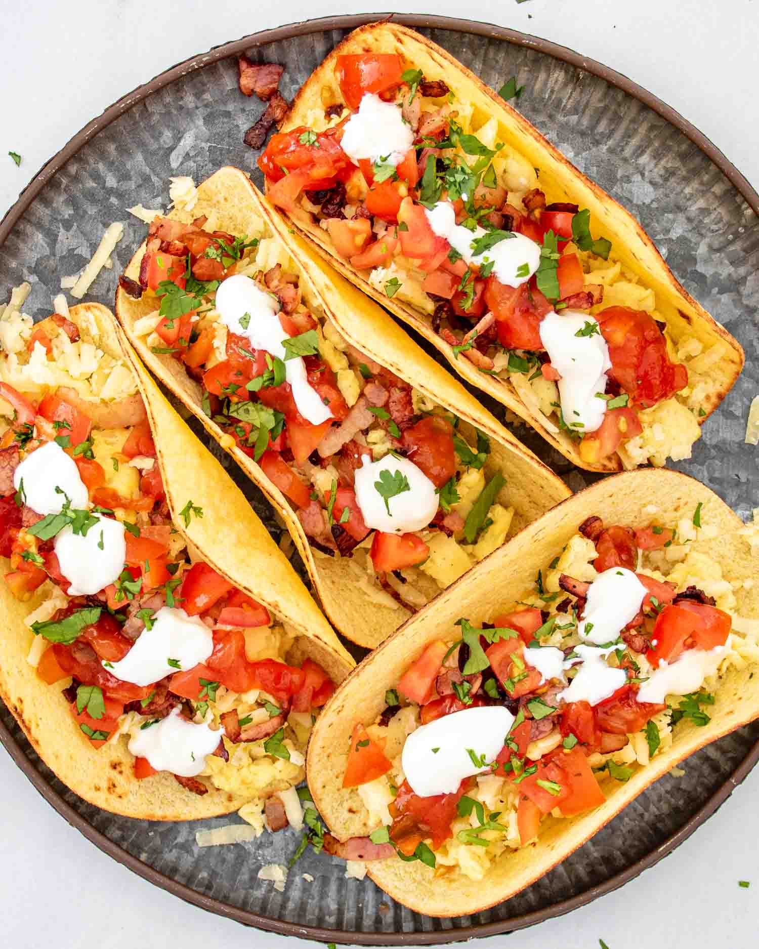 a plate with 4 tacos garnished with sour cream, salsa and cilantro.