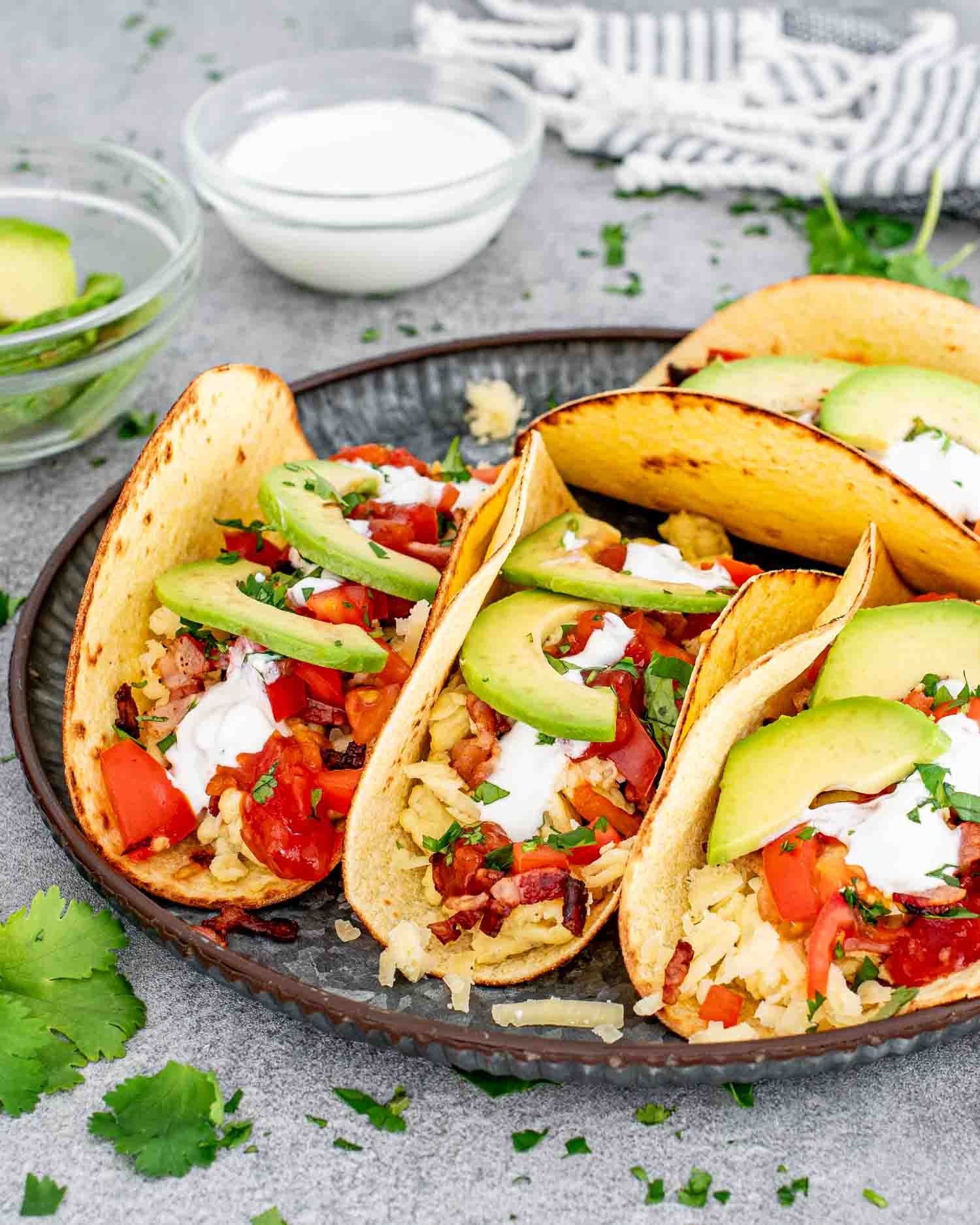 a plate with 4 tacos garnished with sour cream, salsa and avocados.