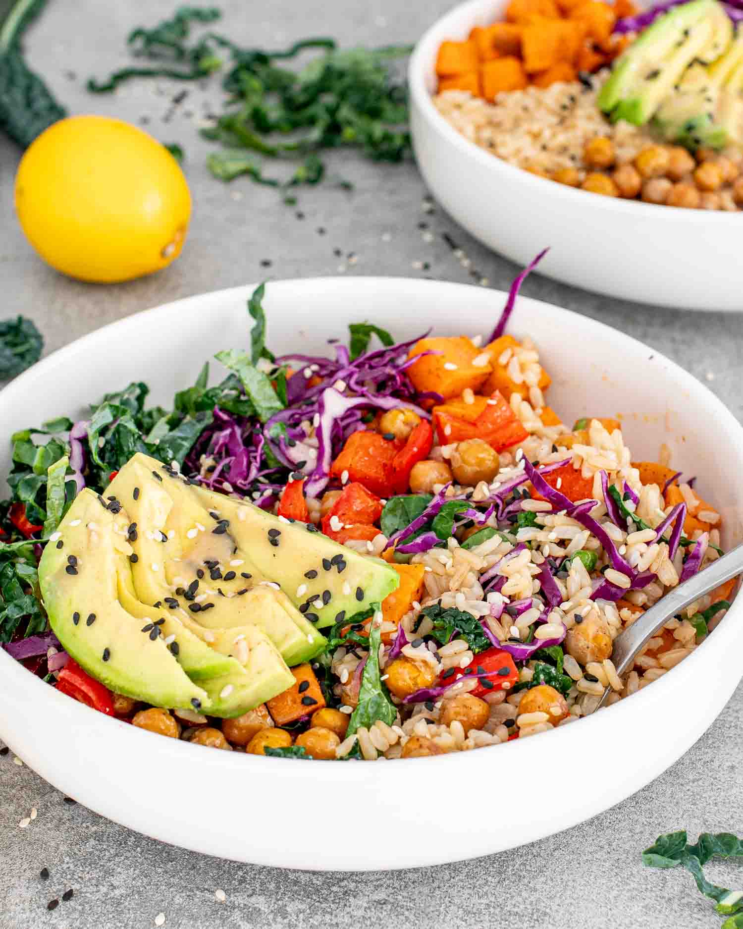 A colorful Buddha bowl with avocado, chickpeas, rice, and mixed vegetables, garnished with black sesame seeds.