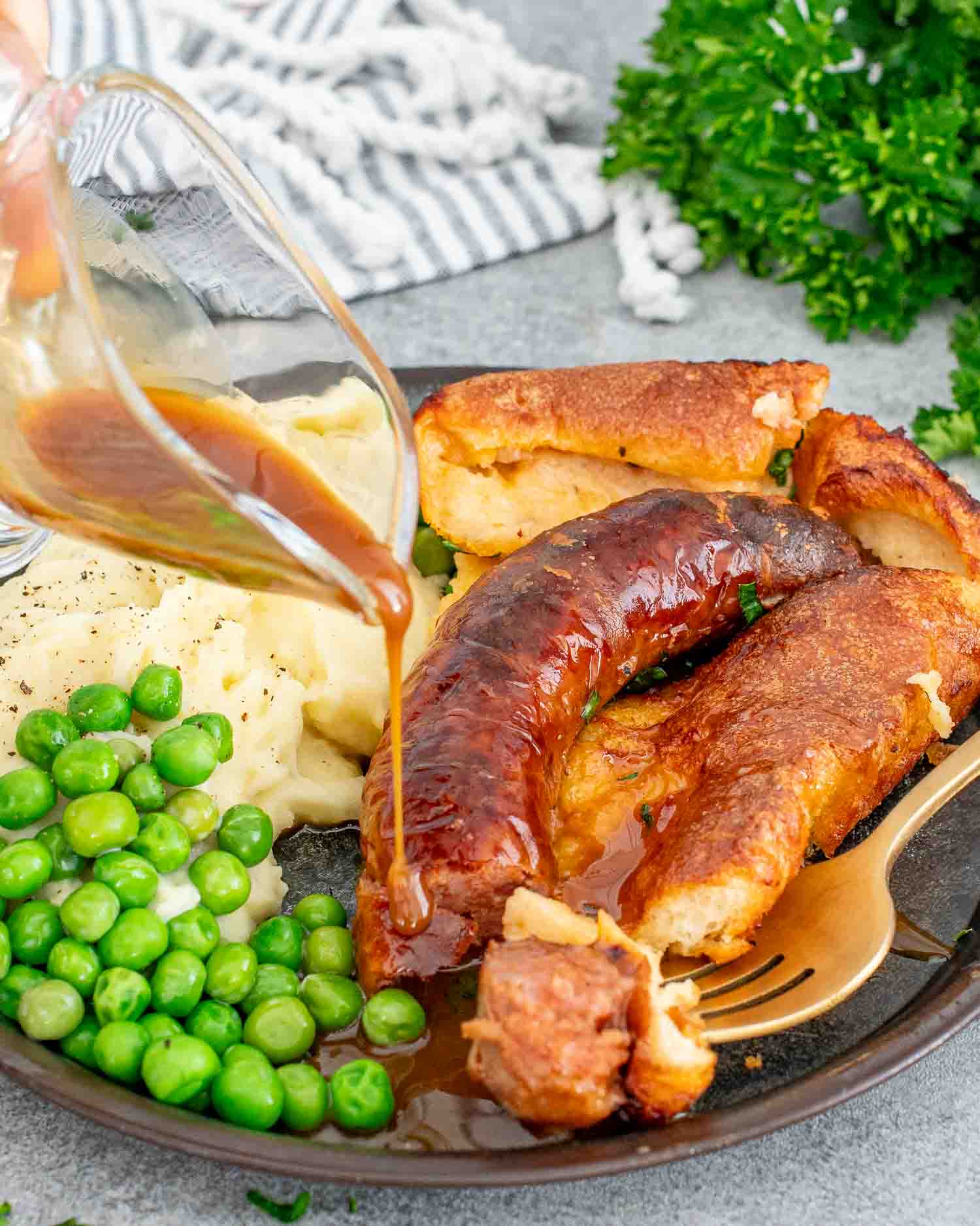 a serving of toad in the hole with gravy along mashed potatoes and peas on a plate.