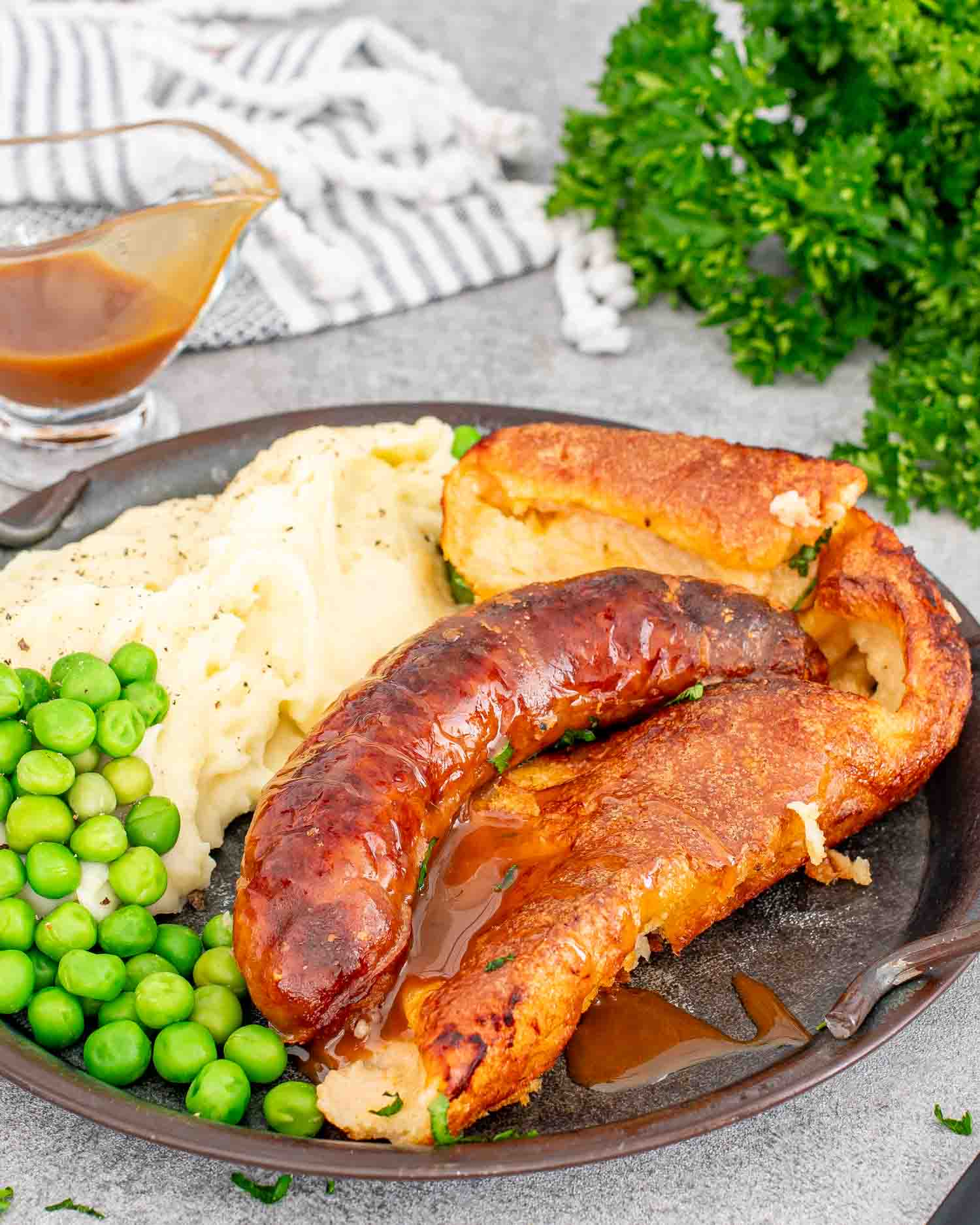 a serving of toad in the hole with gravy along mashed potatoes and peas on a plate.