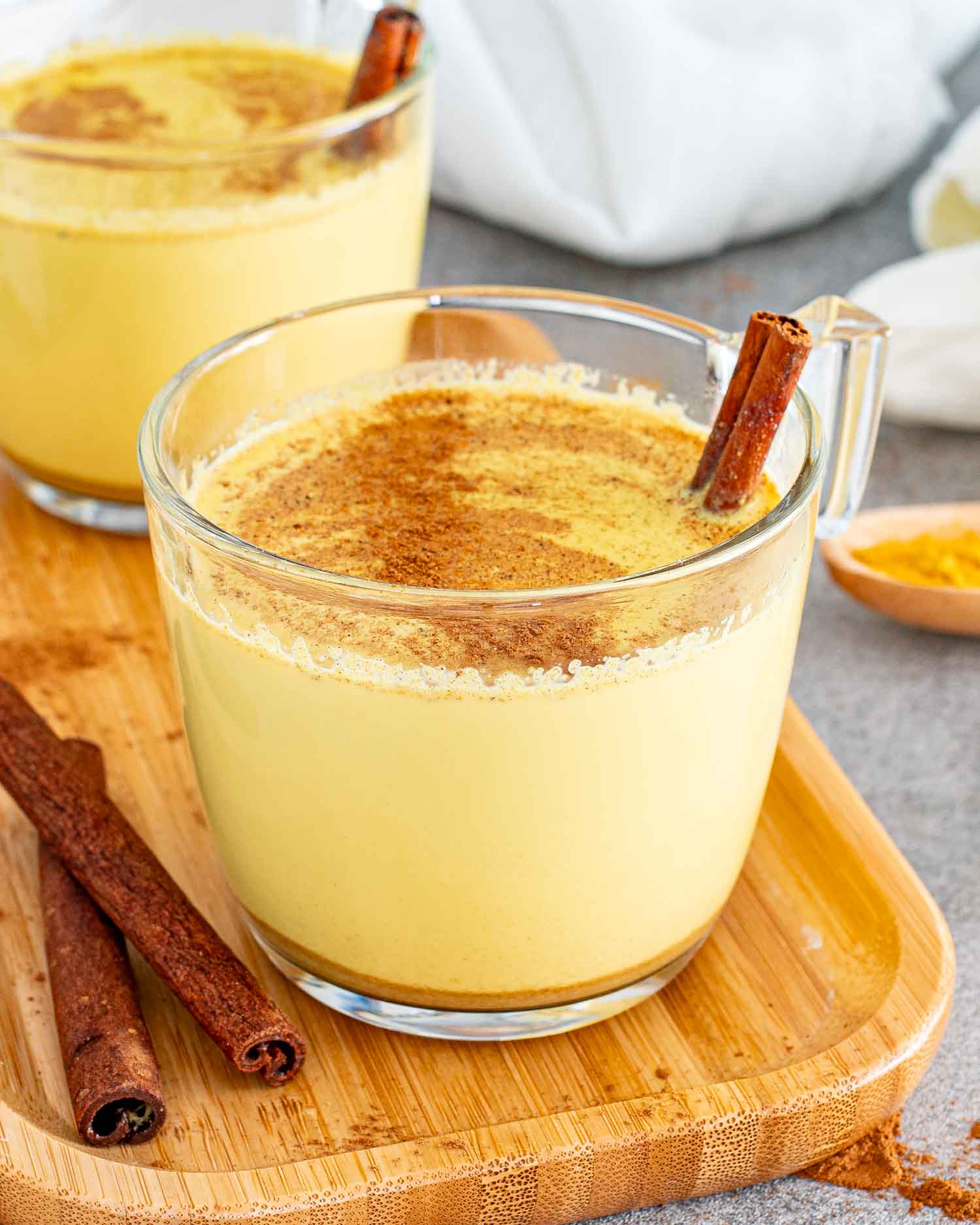 A warm turmeric latte garnished with a dusting of cinnamon and a whole cinnamon stick.