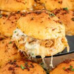 Golden-brown buffalo chicken sliders in a baking dish topped with melted cheese and parsley, freshly baked and ready to enjoy.