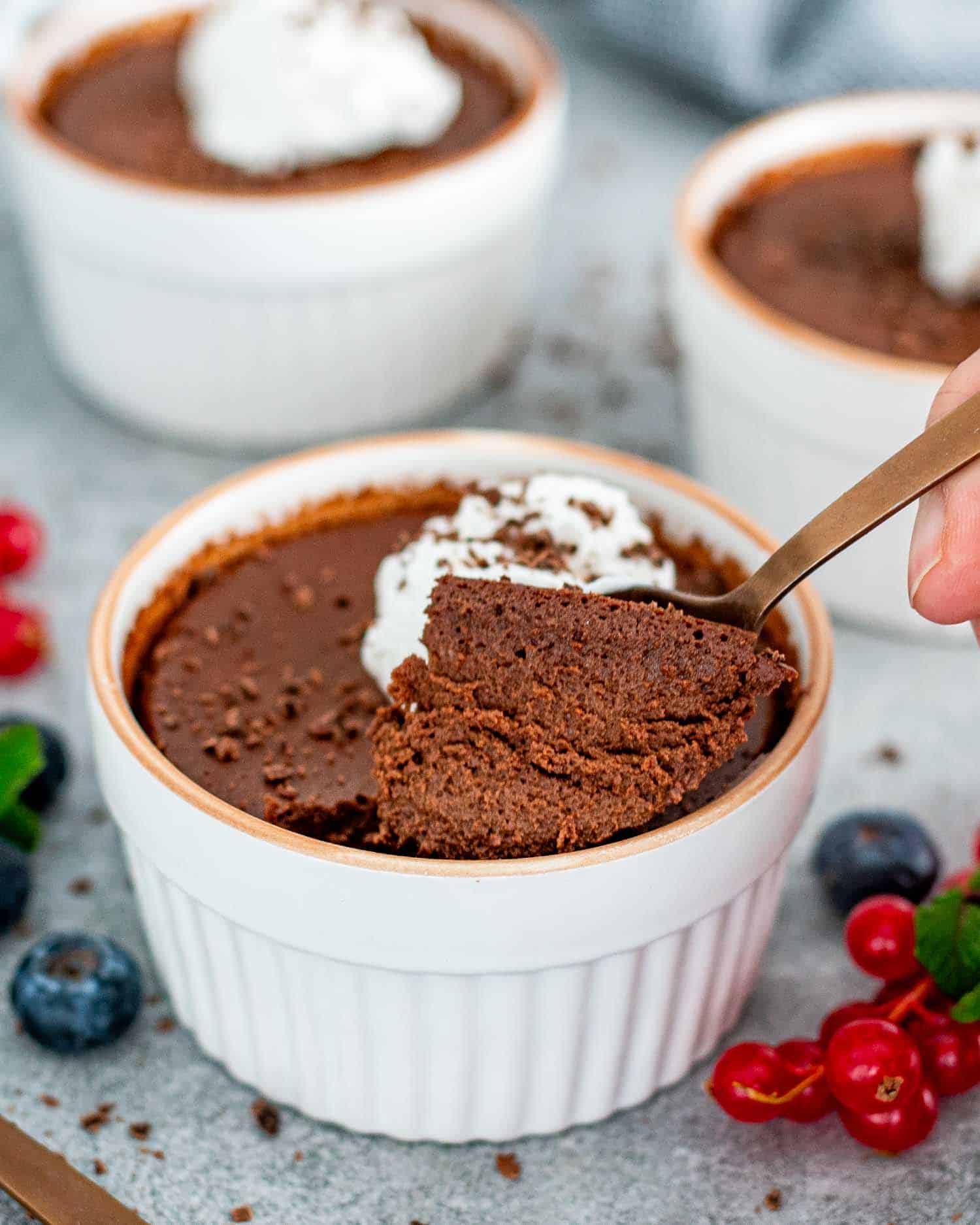 Chocolate pots de crème topped with whipped cream, garnished with fresh berries and chocolate shavings.