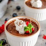 Chocolate pots de crème topped with whipped cream, garnished with fresh berries and chocolate shavings.