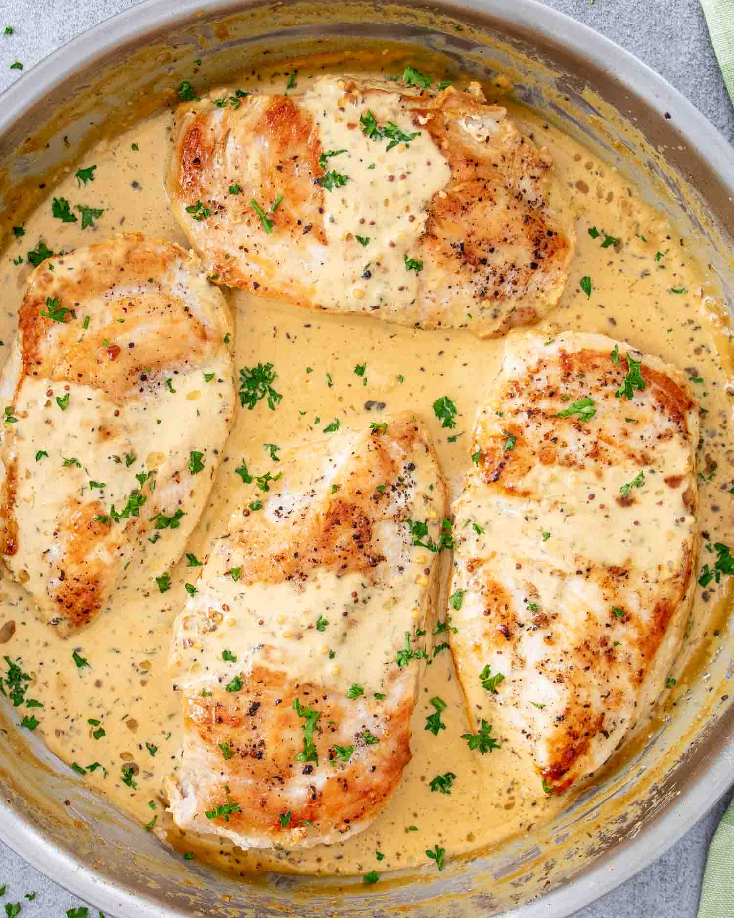 freshly made creamy mustard chicken in a skillet garnished with parsley.