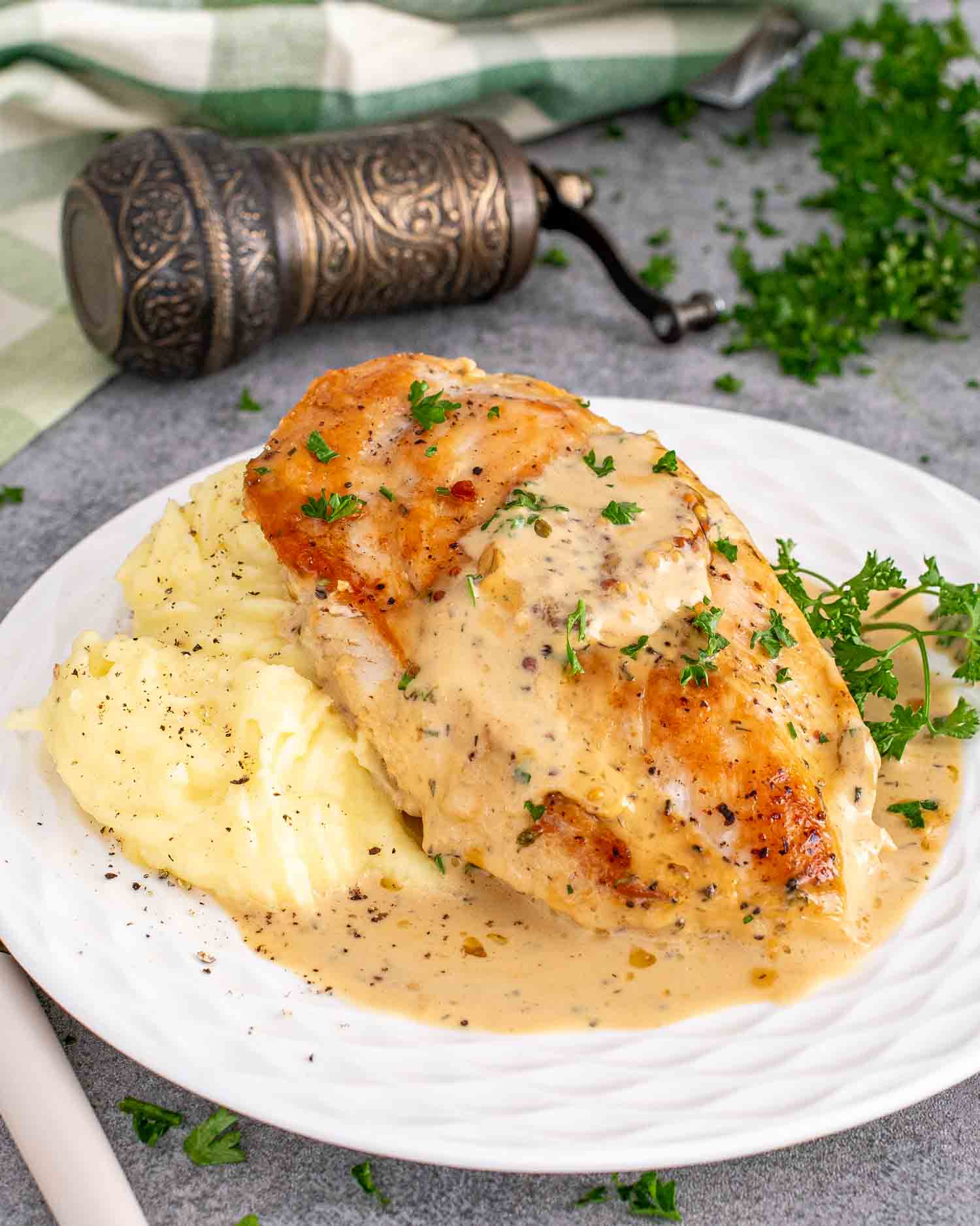 a serving of creamy mustard chicken breast along side some mashed potatoes garnished with parsley.