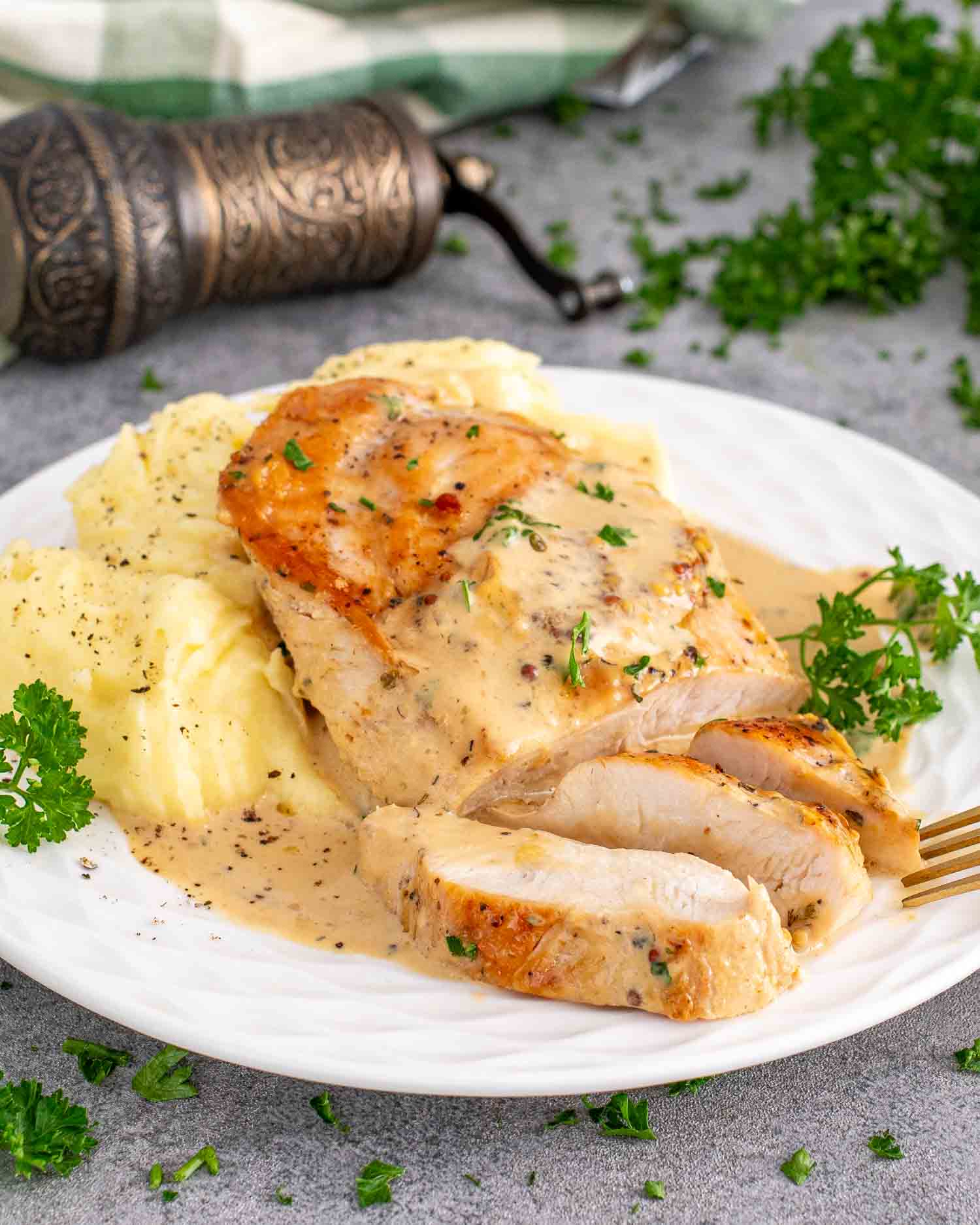 a serving of creamy mustard chicken breast along side some mashed potatoes garnished with parsley.