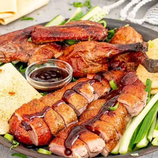 Sliced Peking Duck served with cucumber, green onions, hoisin sauce, and thin pancakes on a plate.